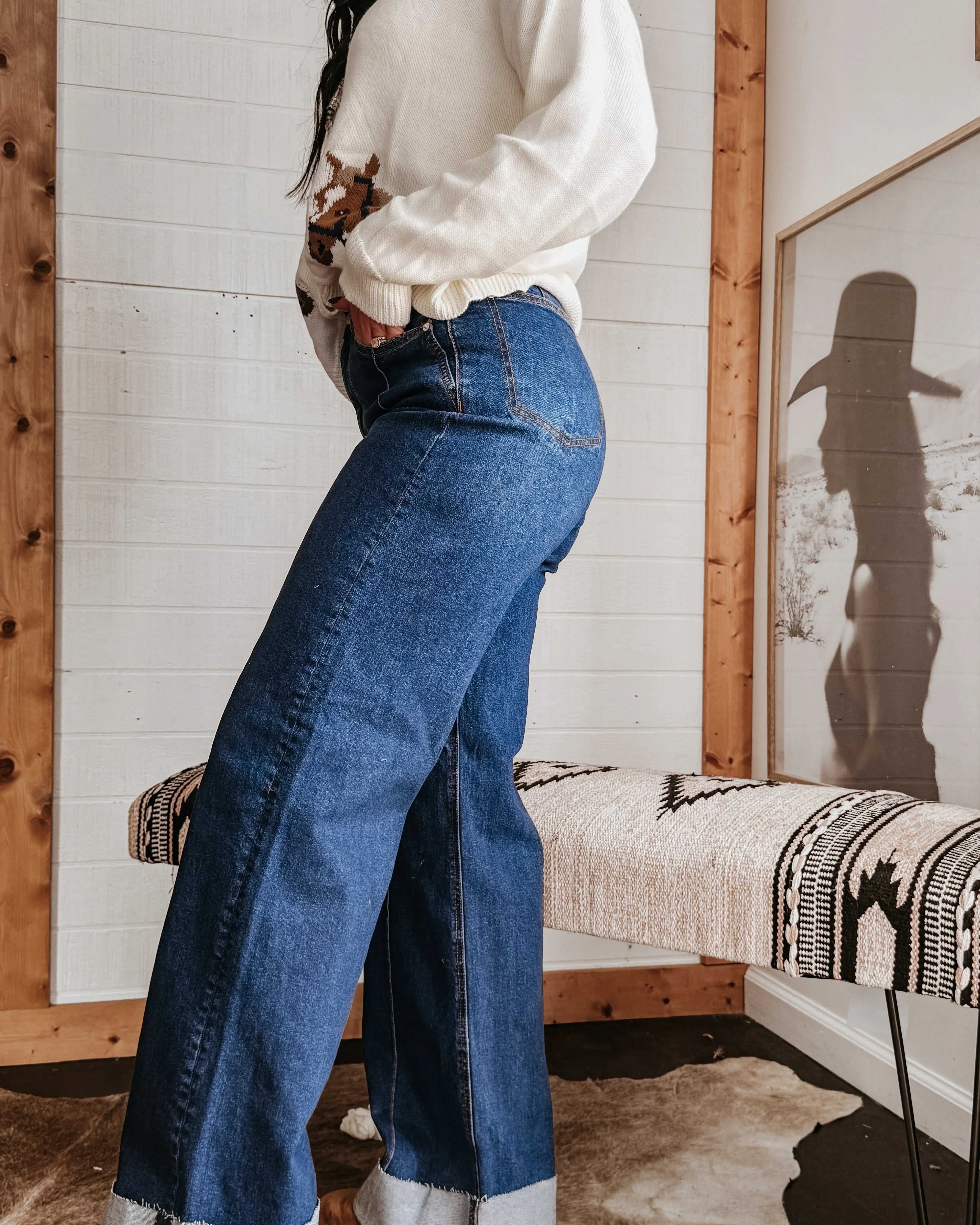 Woman wearing wide leg denim jeans and cow print sweater in western boho styled room