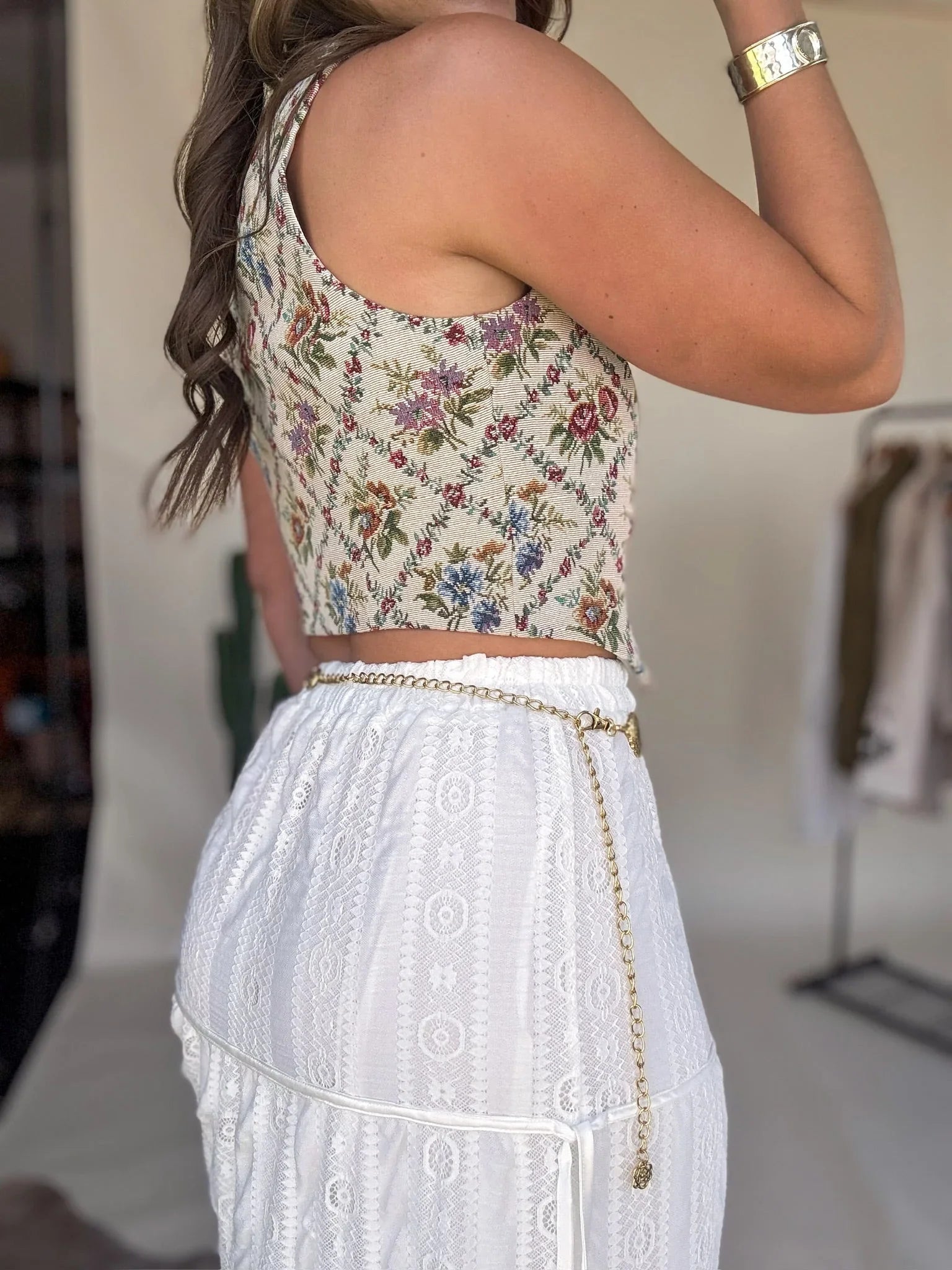 Woman wearing a floral crop top and white skirt with a gold chain belt.