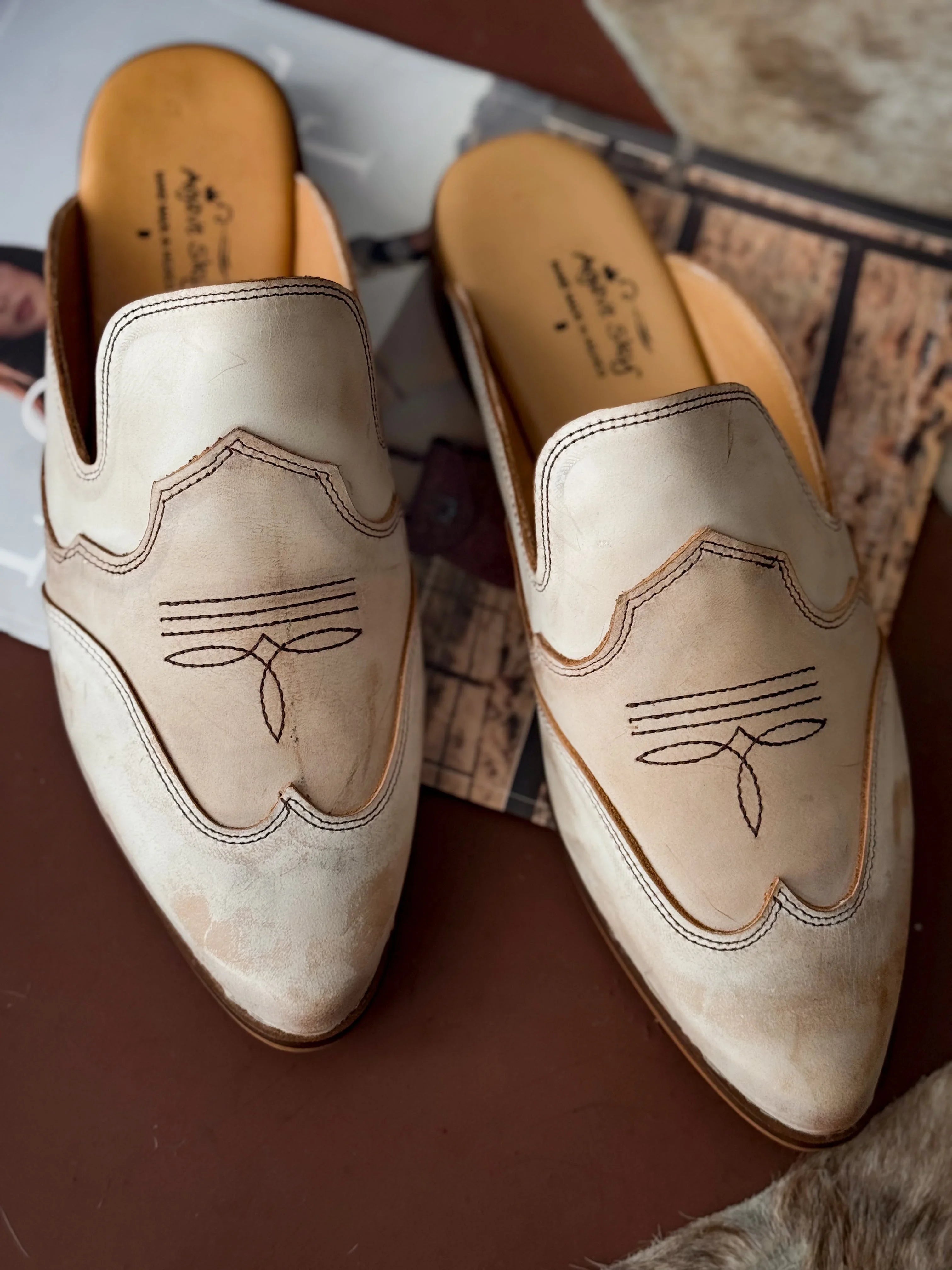 Pair of beige leather shoes with decorative stitching on a textured surface
