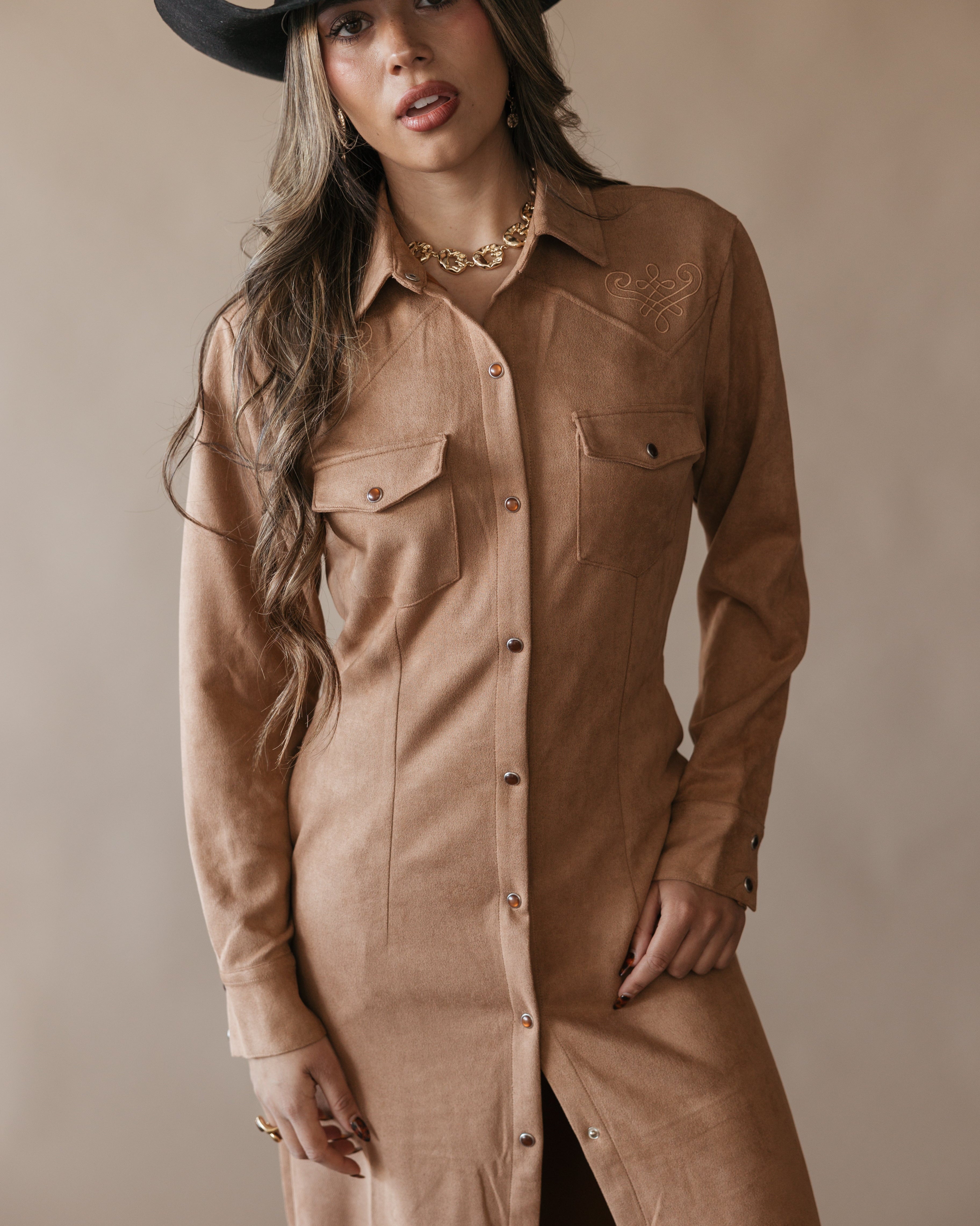 Woman in western suede shirt dress with fringe, cowboy hat, and gold jewelry, boho cowgirl style