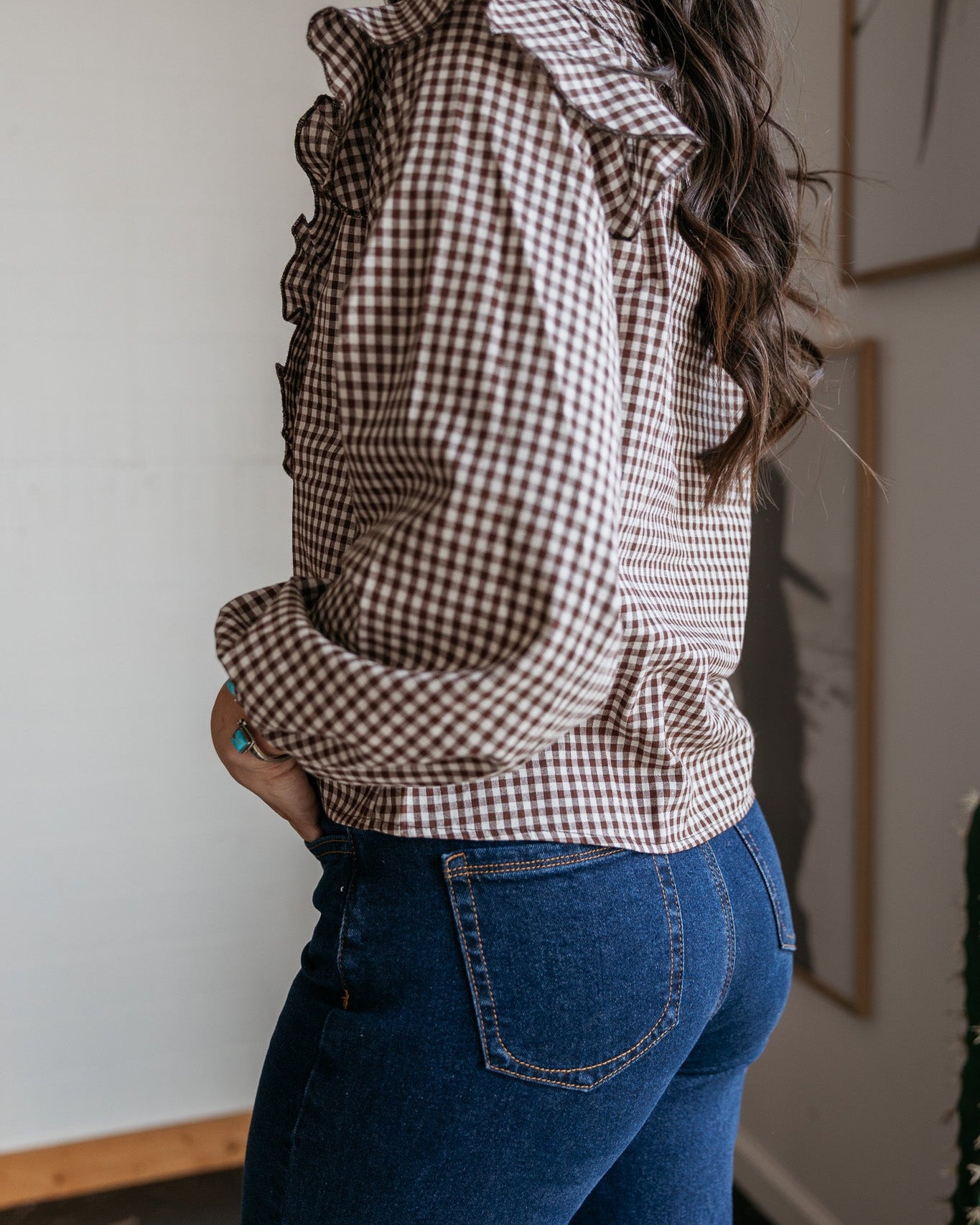 Woman wearing brown gingham ruffle blouse and high-waisted blue jeans, western style