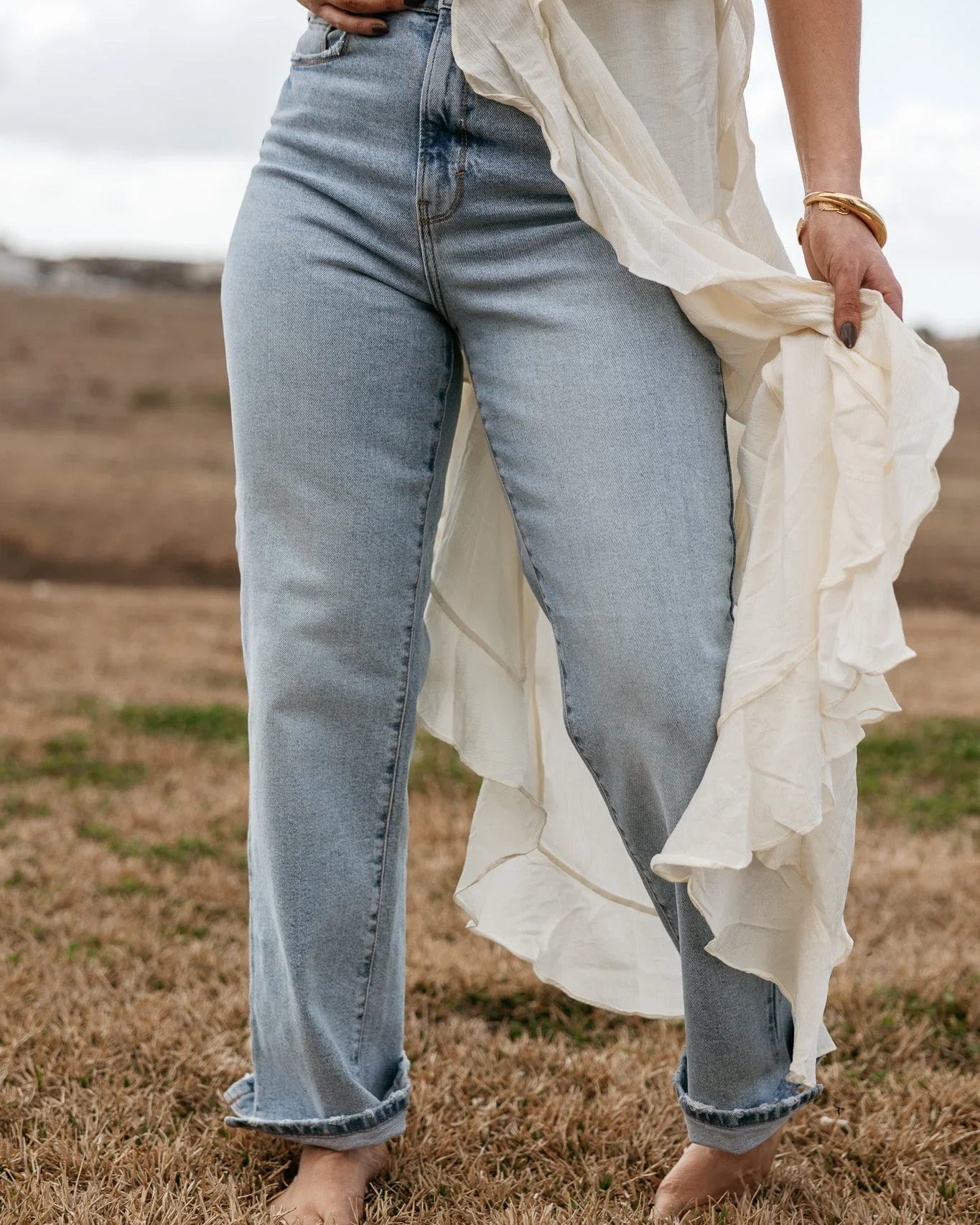 Woman in light wash western jeans and flowy white boho top standing barefoot on grass