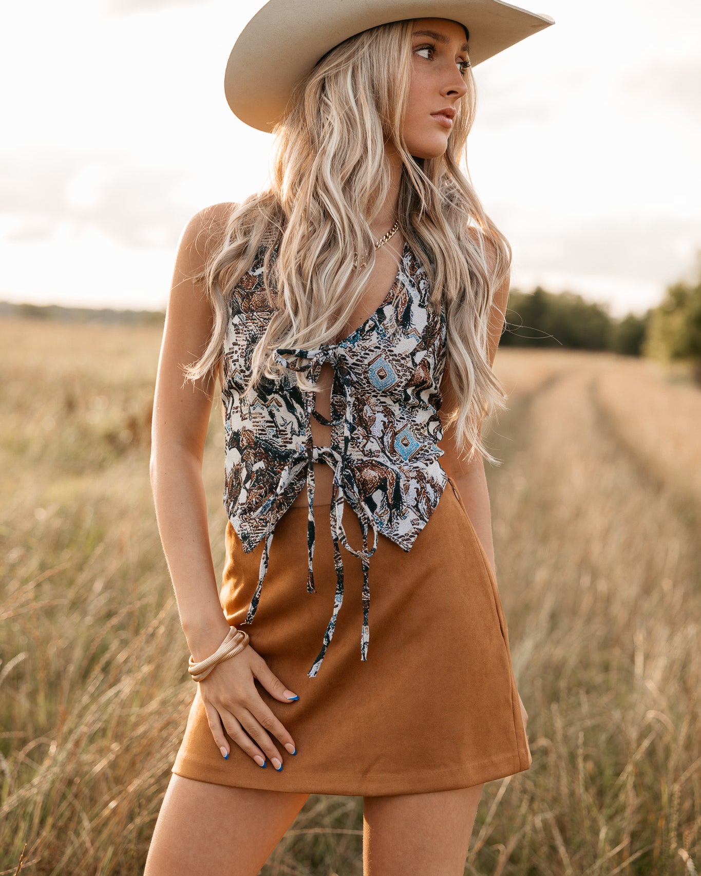 women wearing tie front halter top with western pattern and a camel skirt standing in a field.