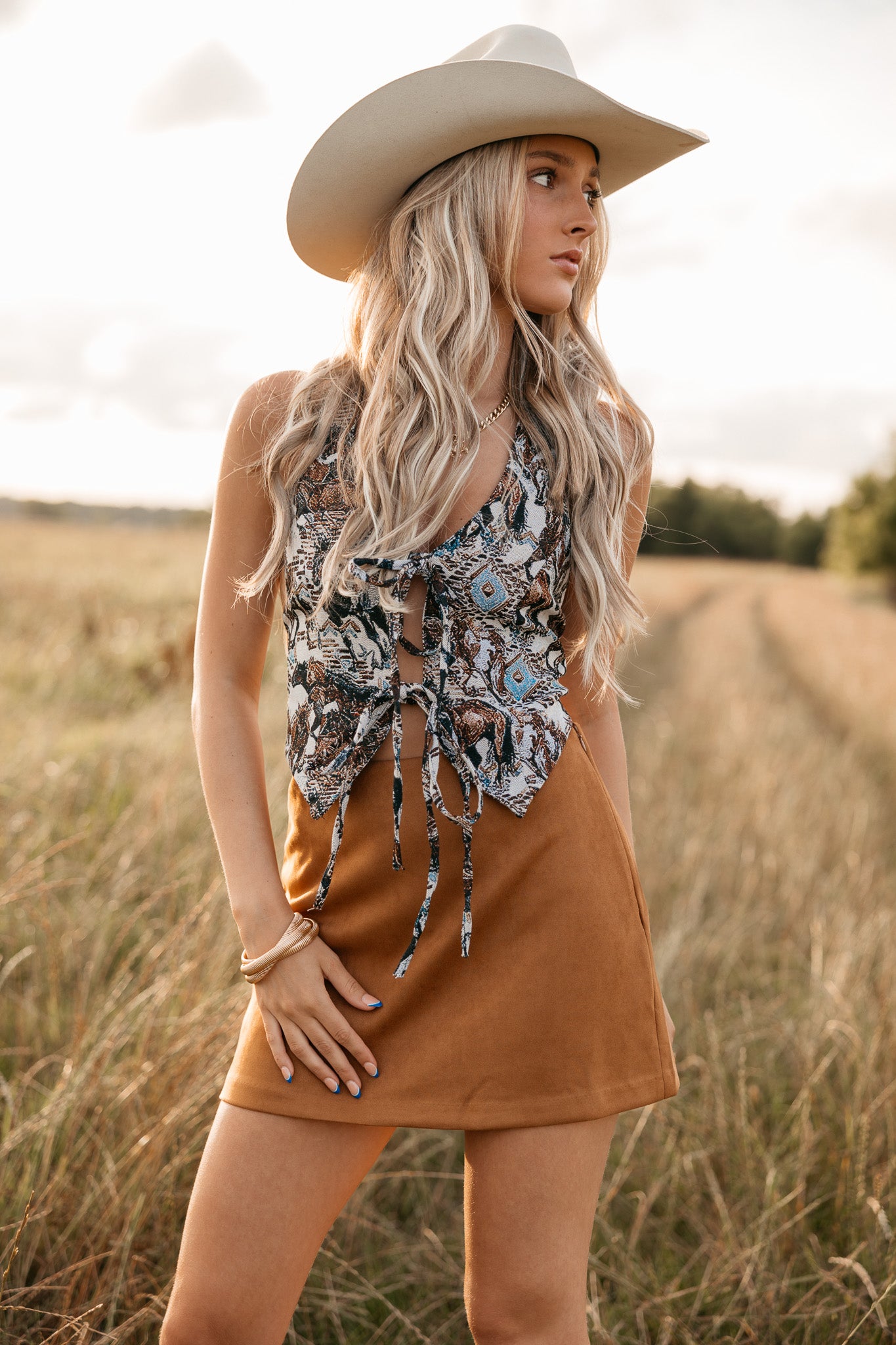 women wearing tie front halter top with western pattern and a camel skirt standing in a field.