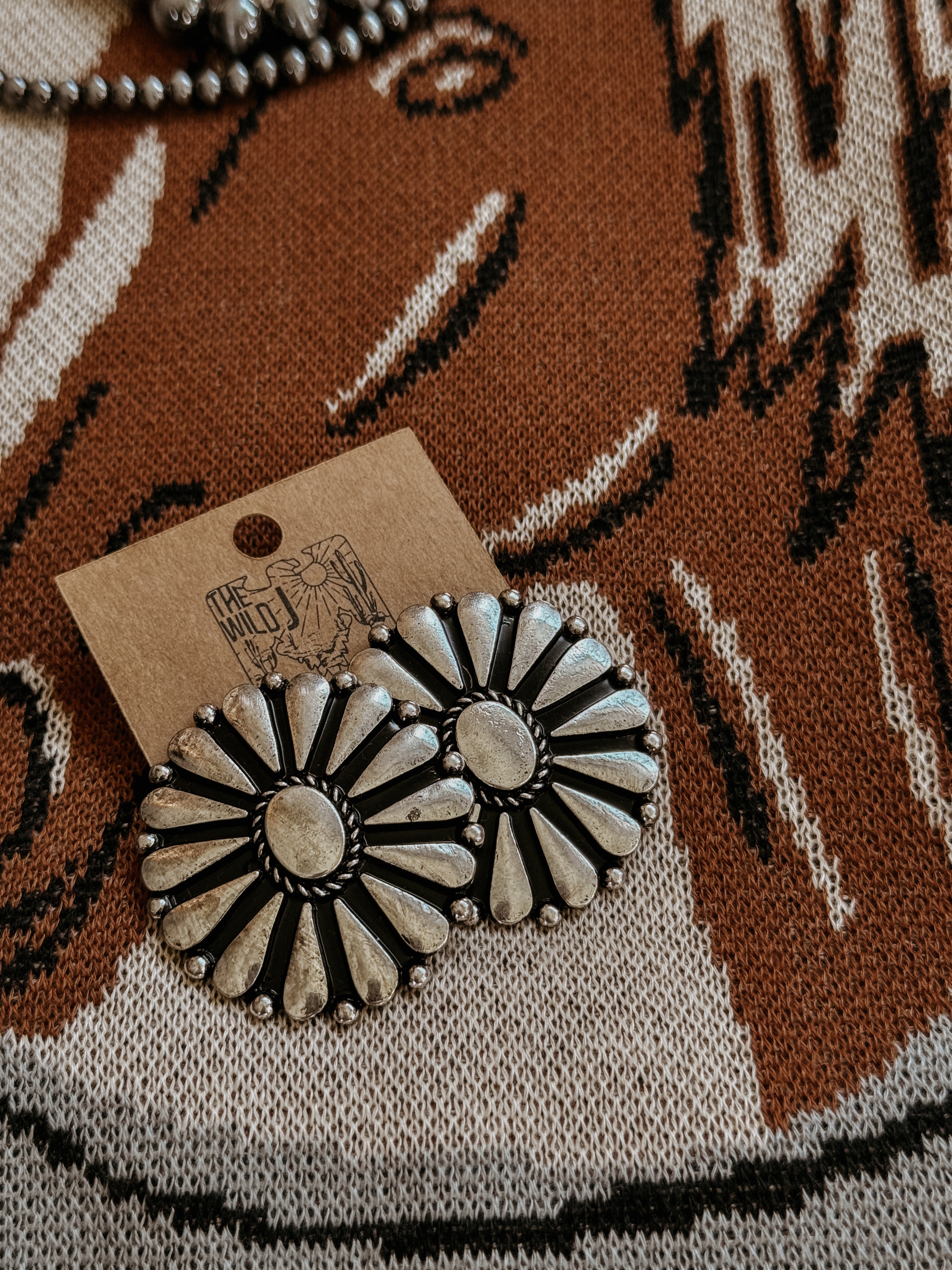 Silver concho stud earrings with floral design on a western knit background