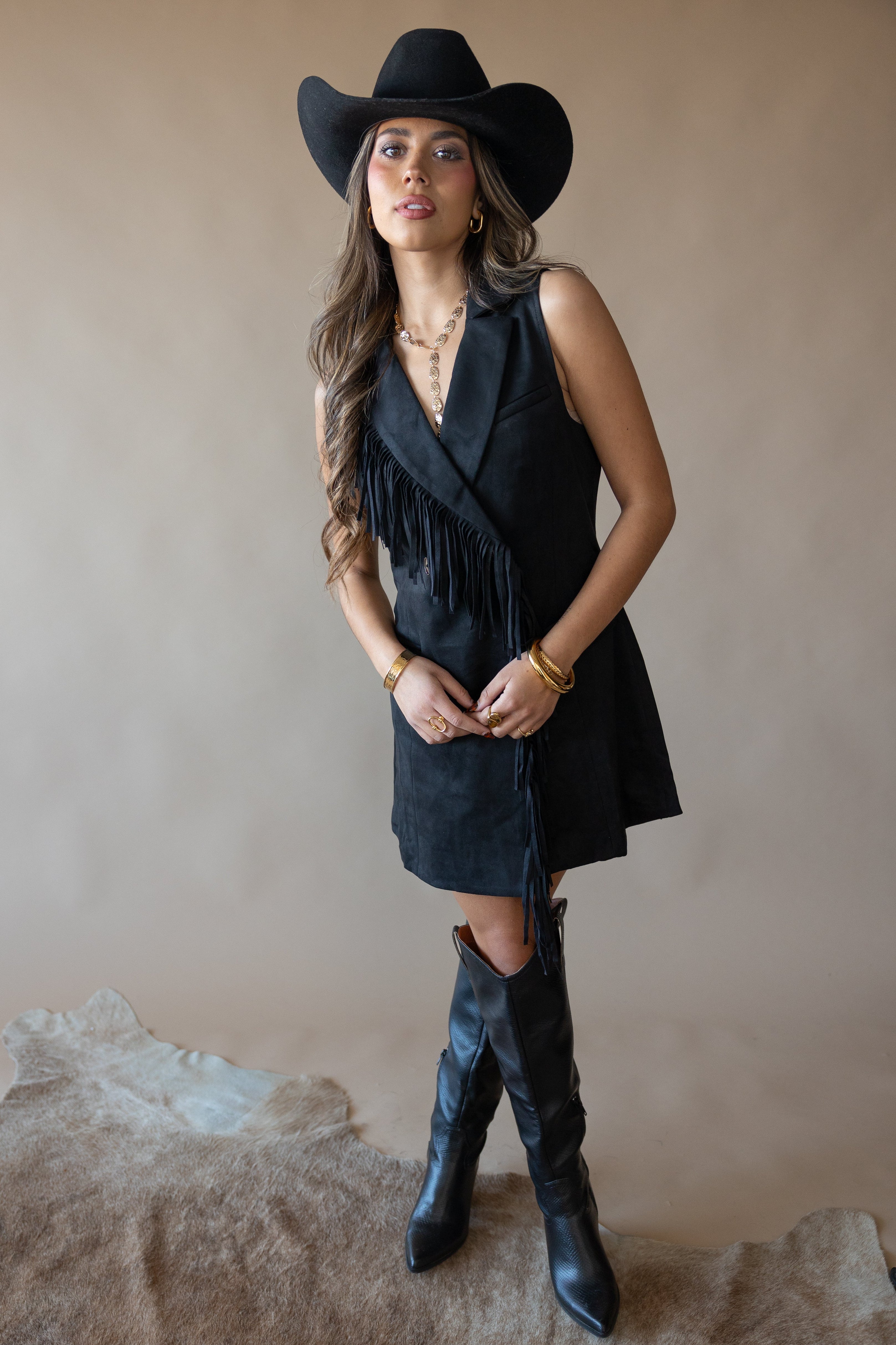 Woman in black cowgirl hat, sleeveless fringe dress, and boots, western boho outfit