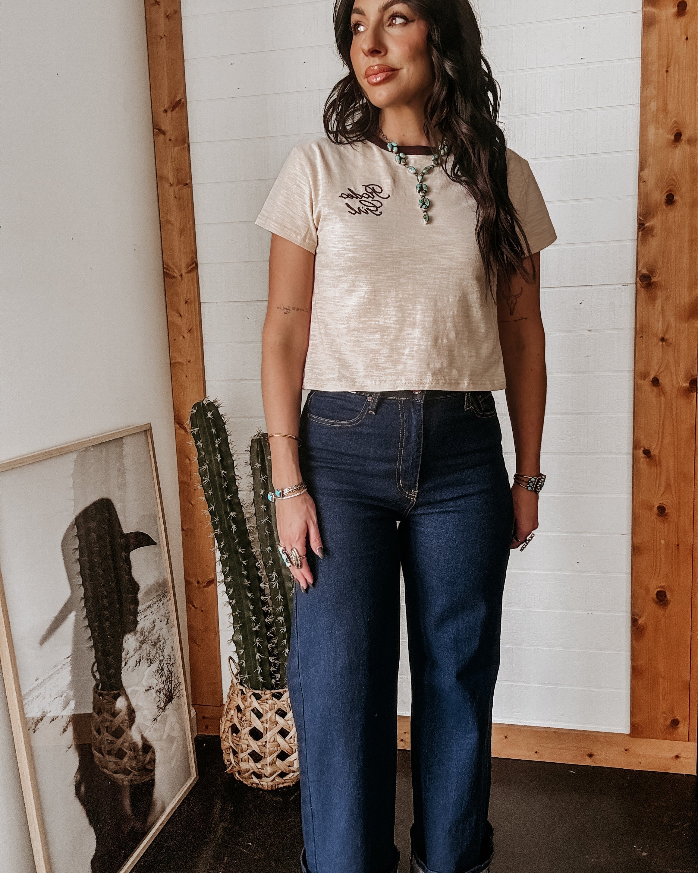 Woman in western boho outfit with graphic tee, turquoise jewelry, and wide leg jeans