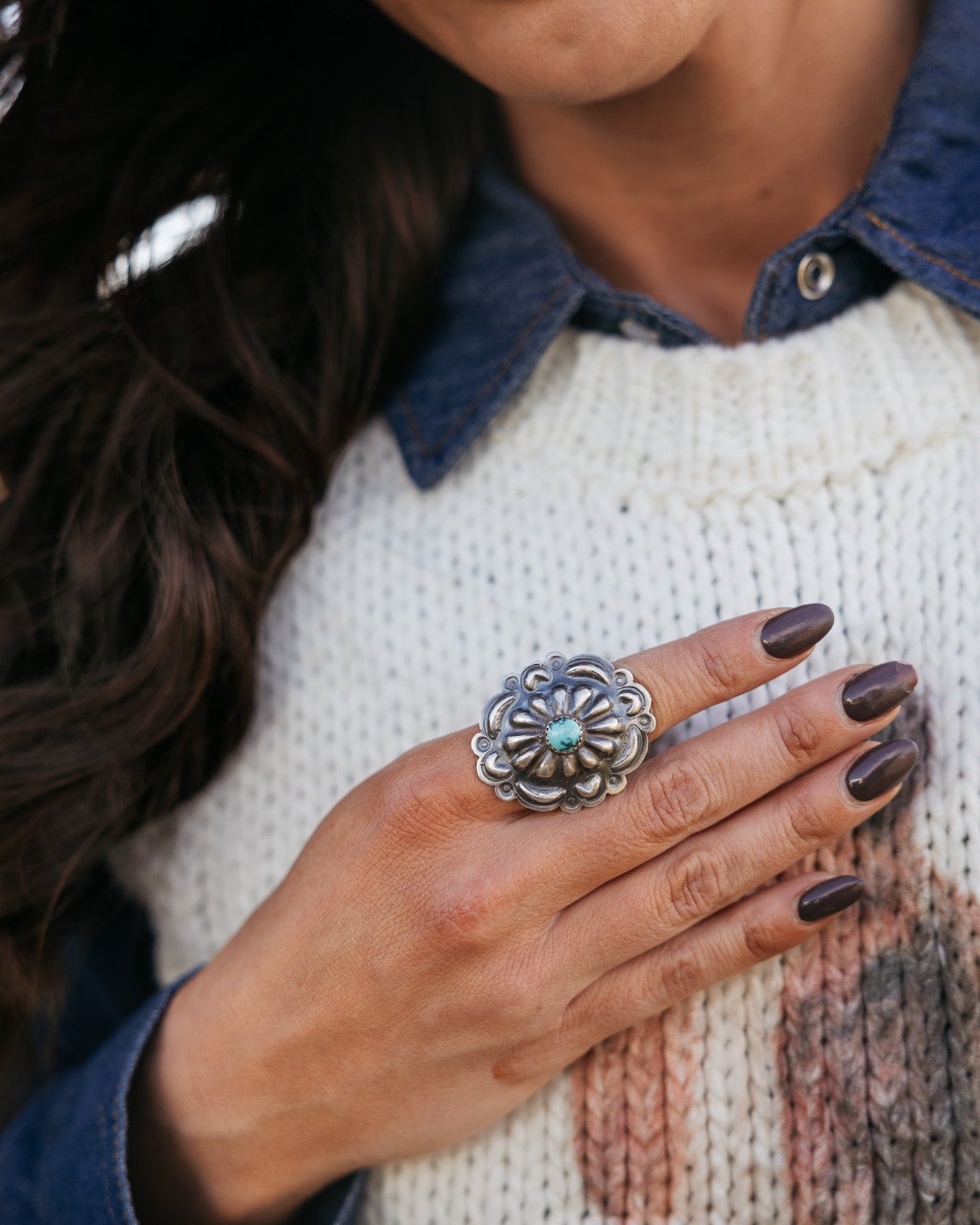 Woman wearing western silver statement ring with turquoise stone, denim shirt, and knit sweater
