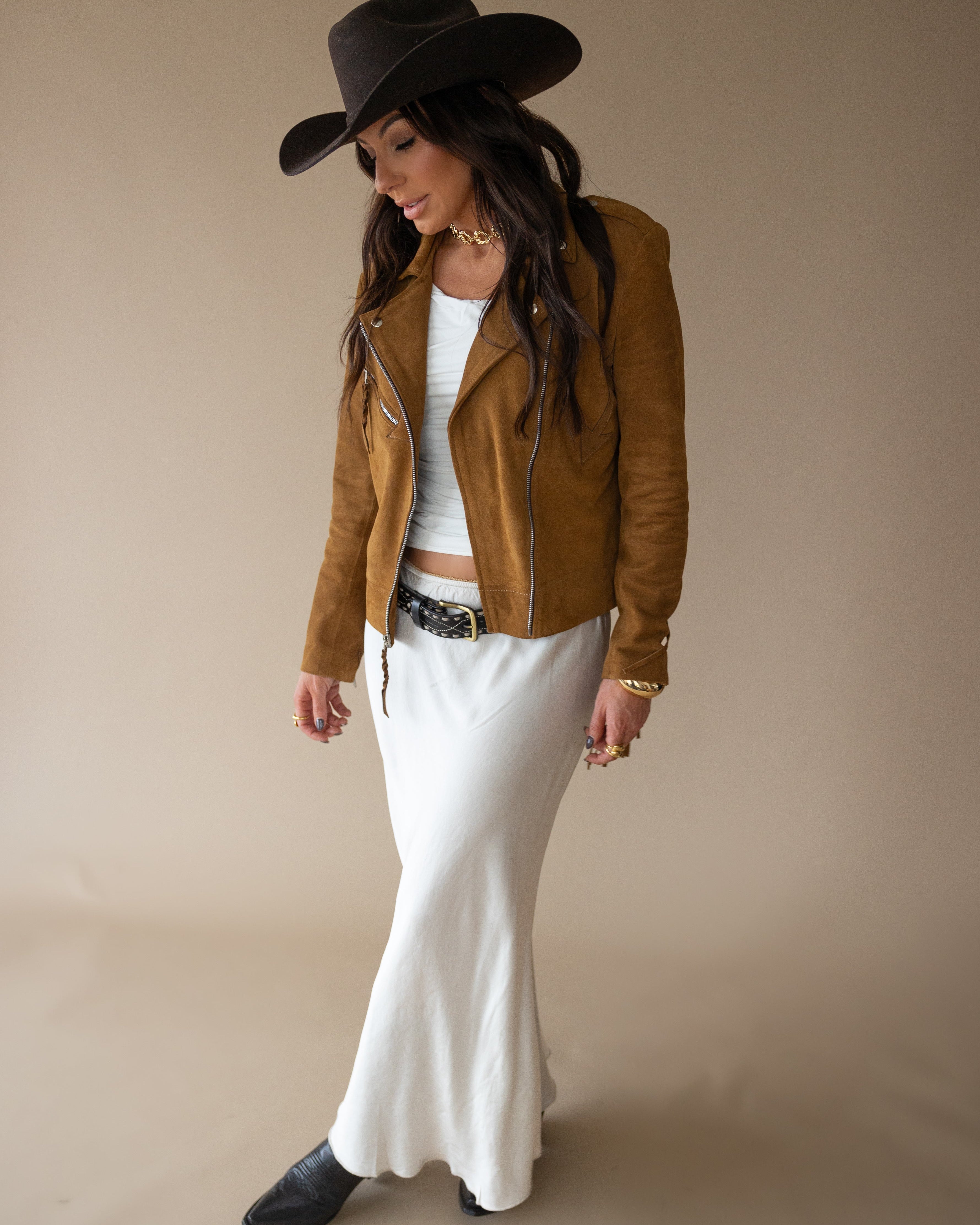 Woman in cowgirl hat, brown suede jacket, white maxi skirt, Western boho outfit