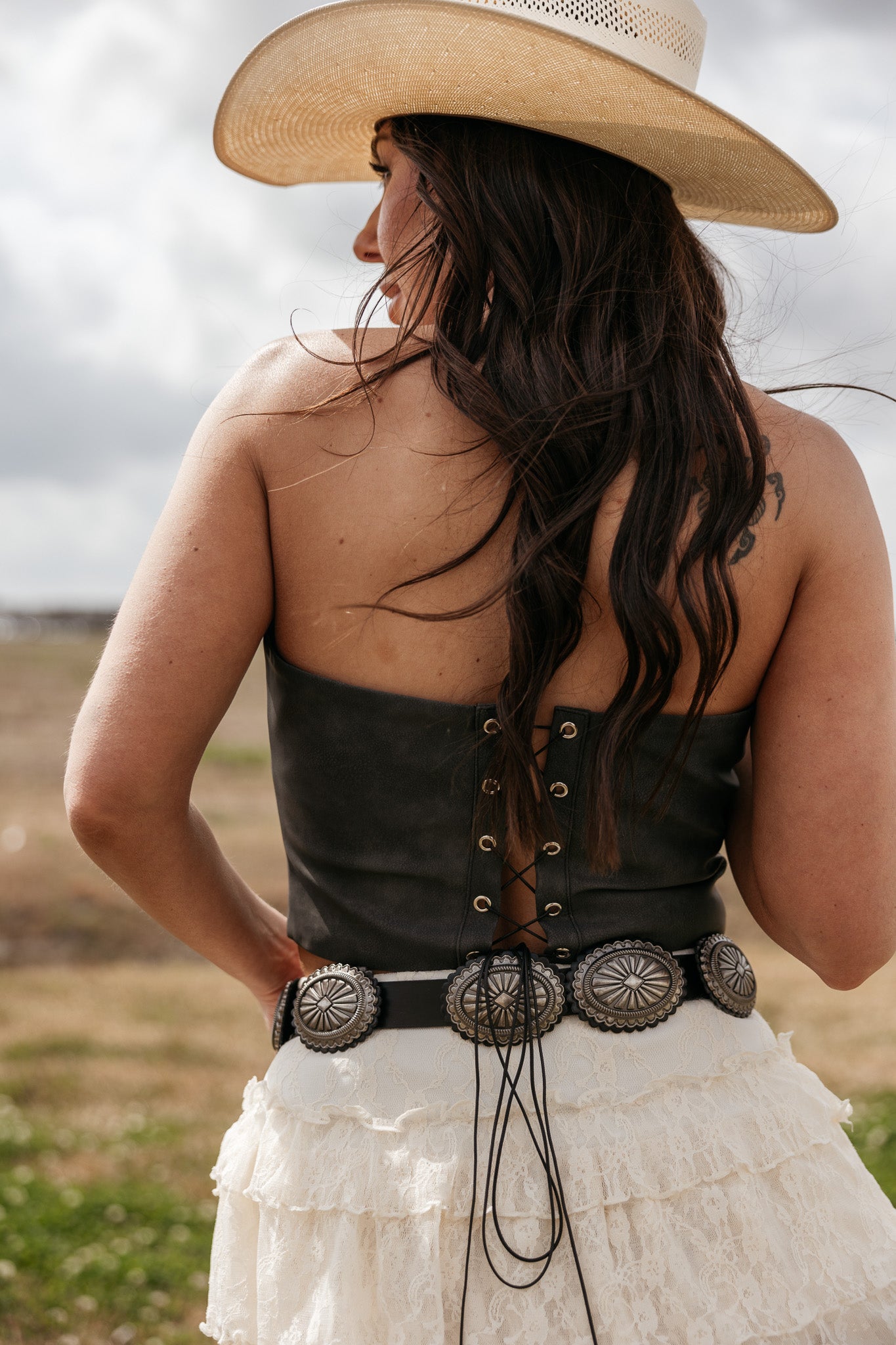 Woman in western boho outfit with cowboy hat, lace skirt, concho belt, and corset top outdoors