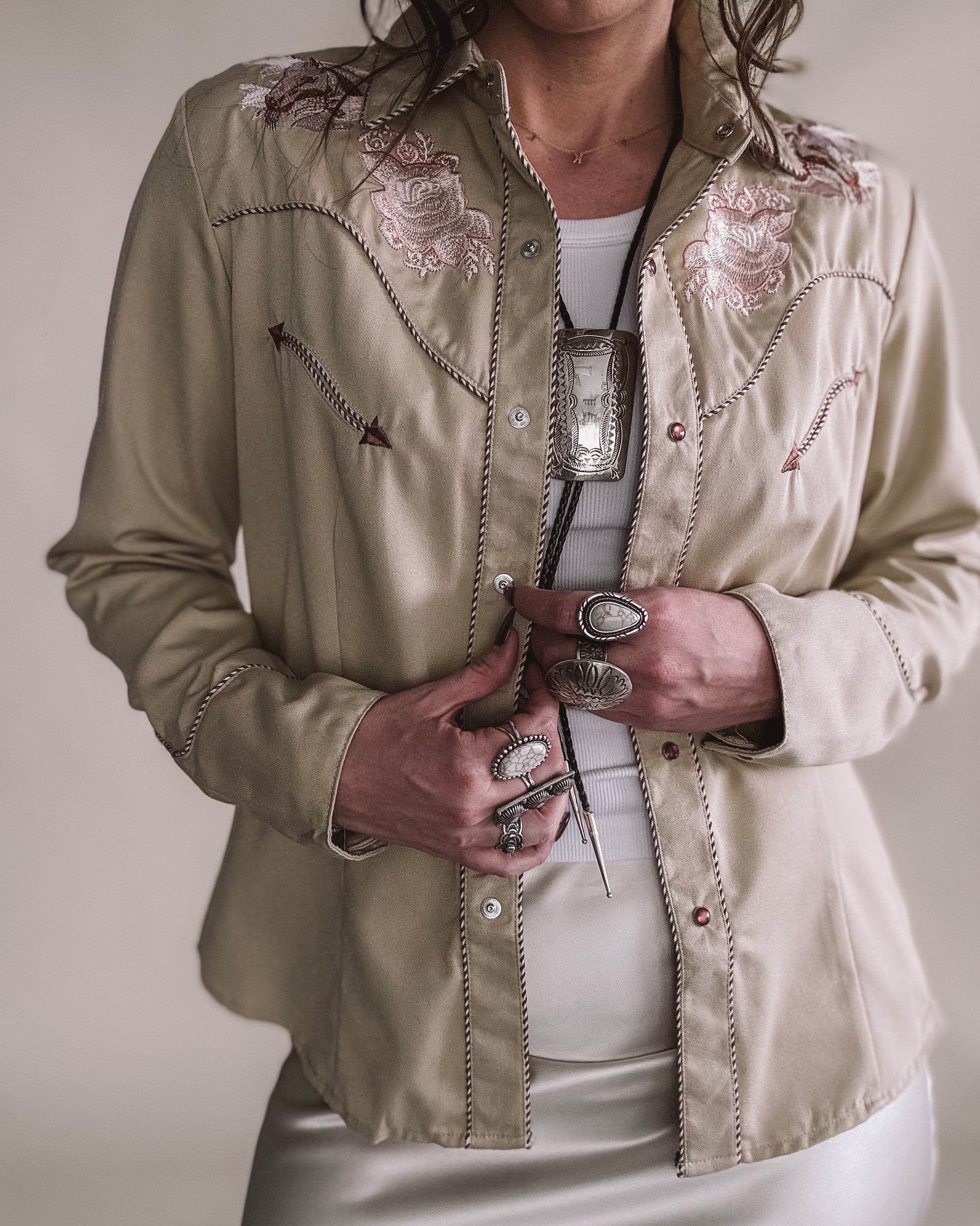 Woman wearing beige embroidered western shirt, silver jewelry, and bolo tie, western fashion