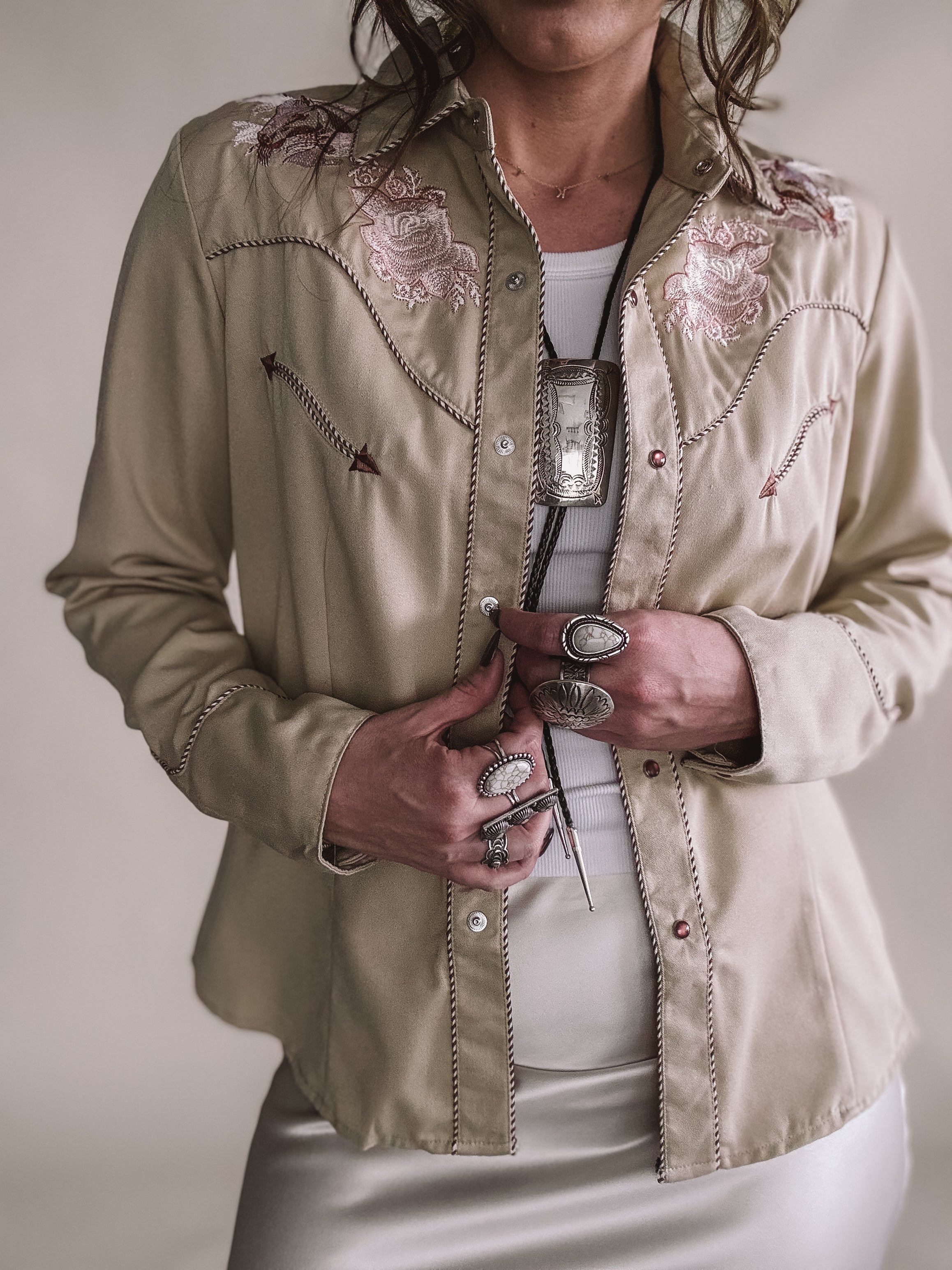 Woman wearing beige embroidered western shirt, silver jewelry, and bolo tie, western fashion