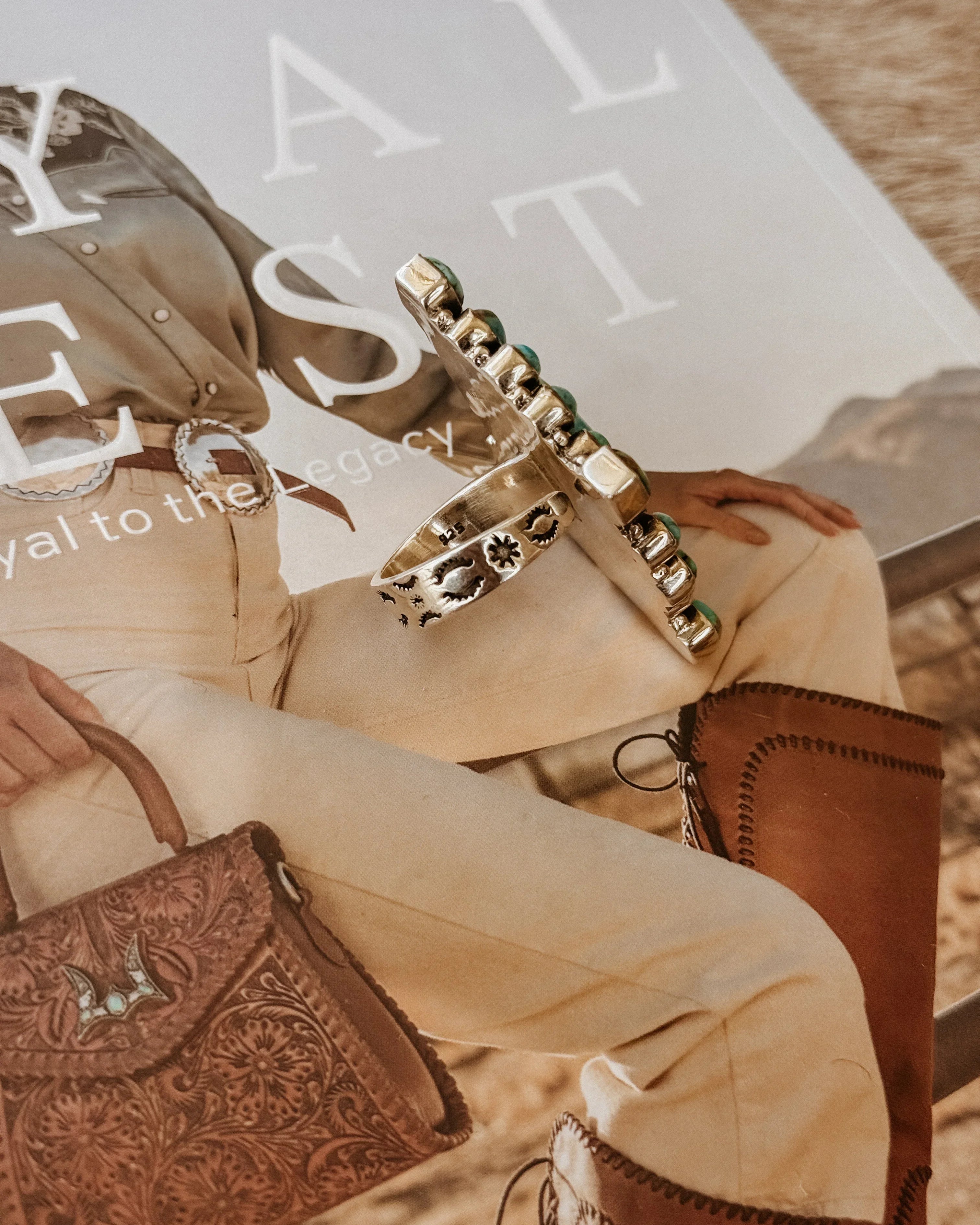 Western silver turquoise ring on magazine with cowgirl outfit, leather purse, and boots