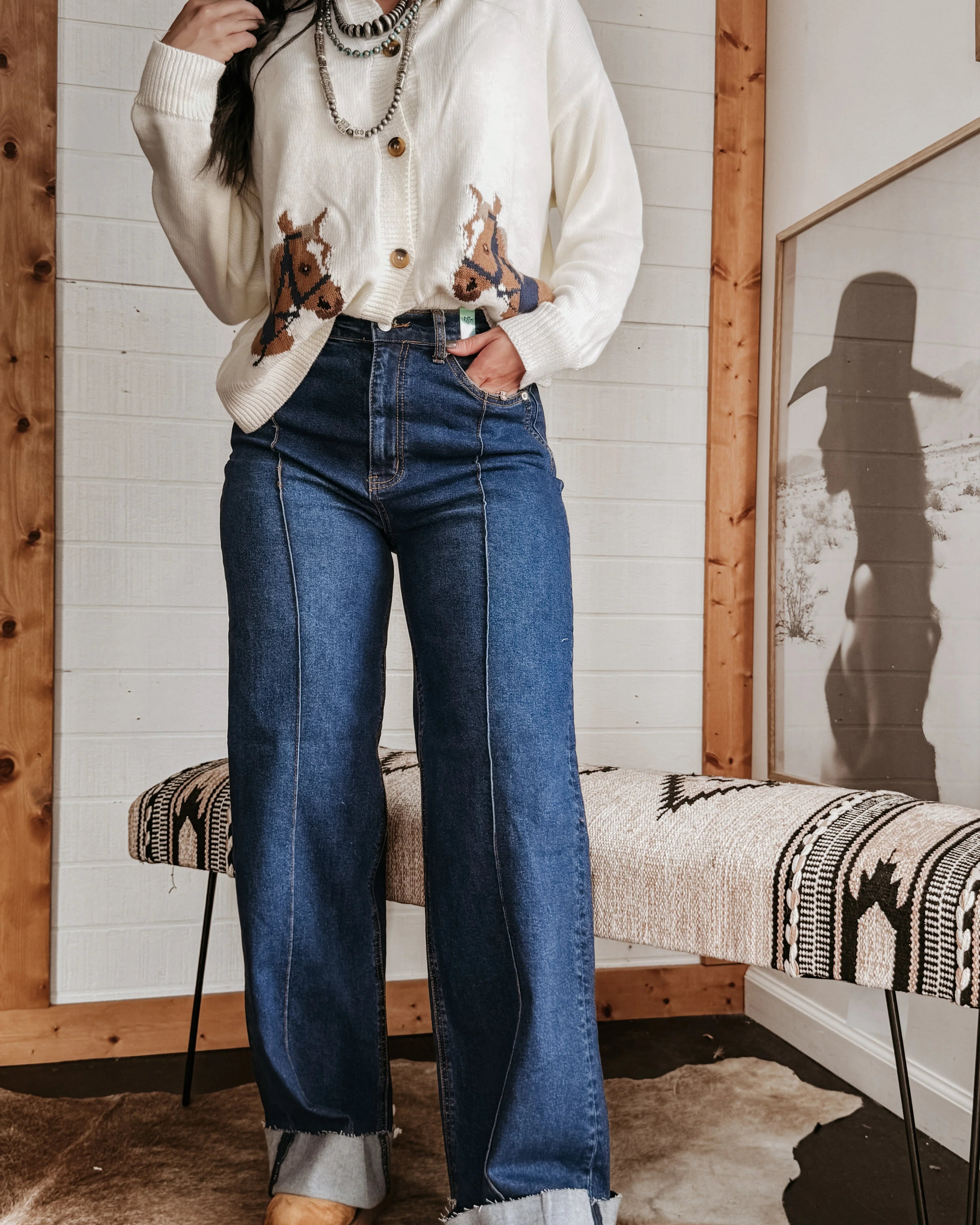 Woman in western boho outfit with horse print sweater, chunky necklace, and wide leg jeans