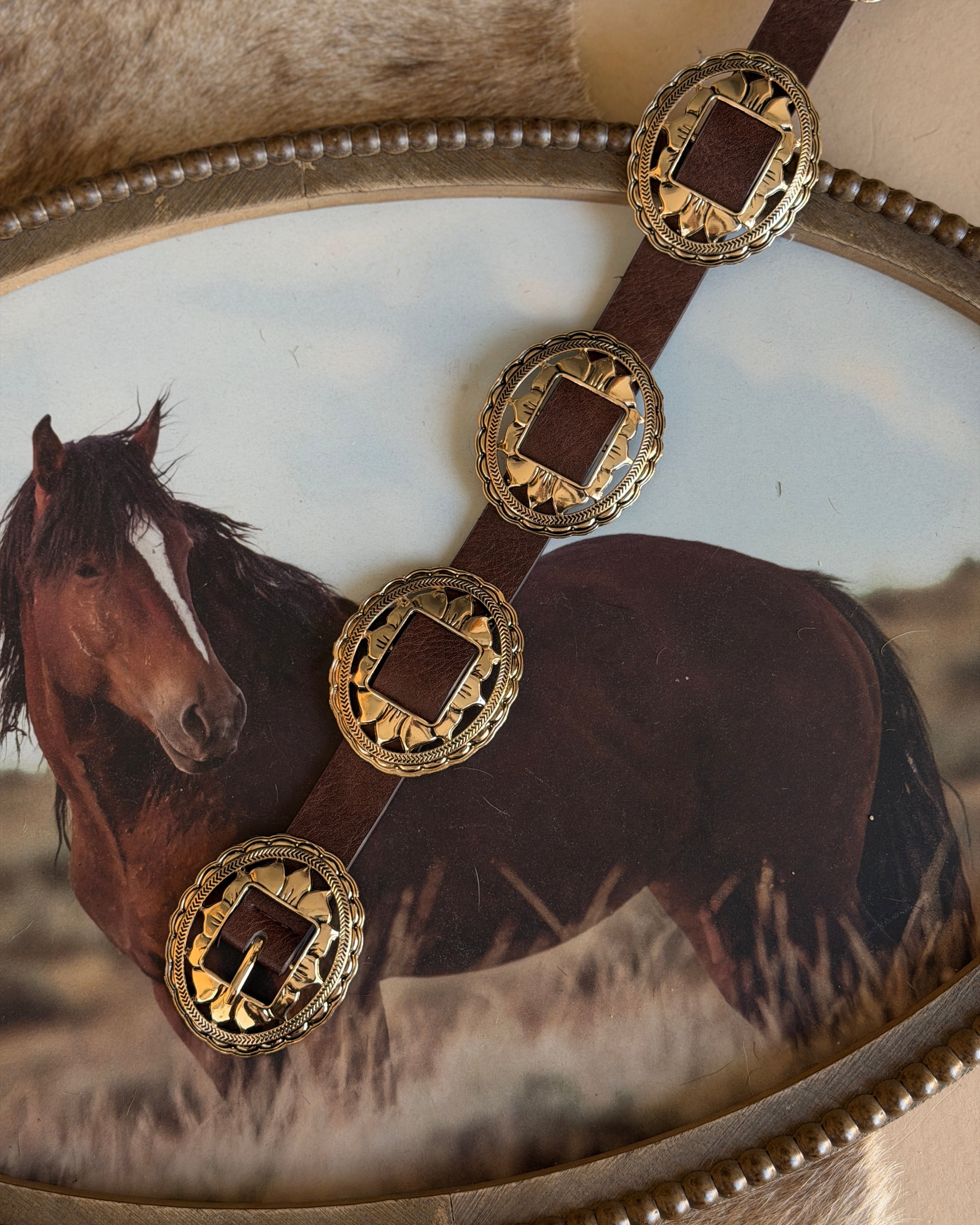 Western concho belt with engraved gold accents on brown leather, rustic cowgirl style