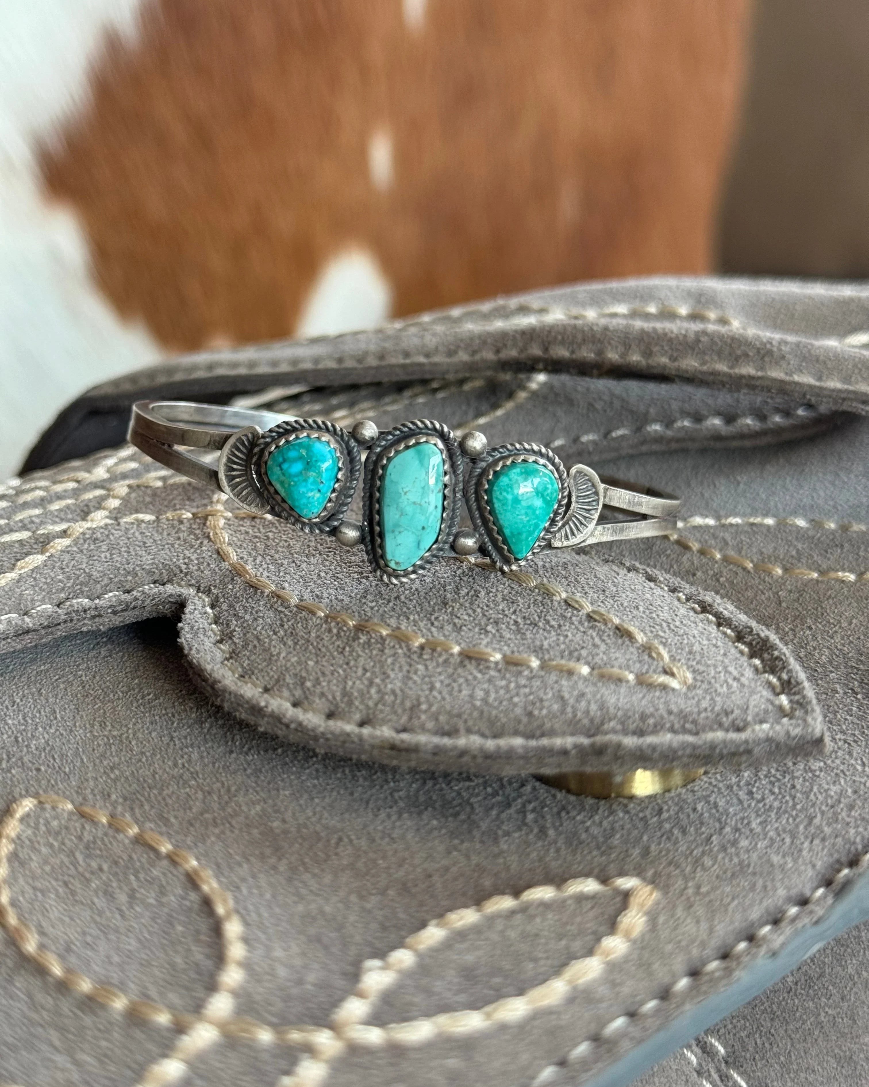 Turquoise silver western cuff bracelet on stitched gray suede with cowhide background