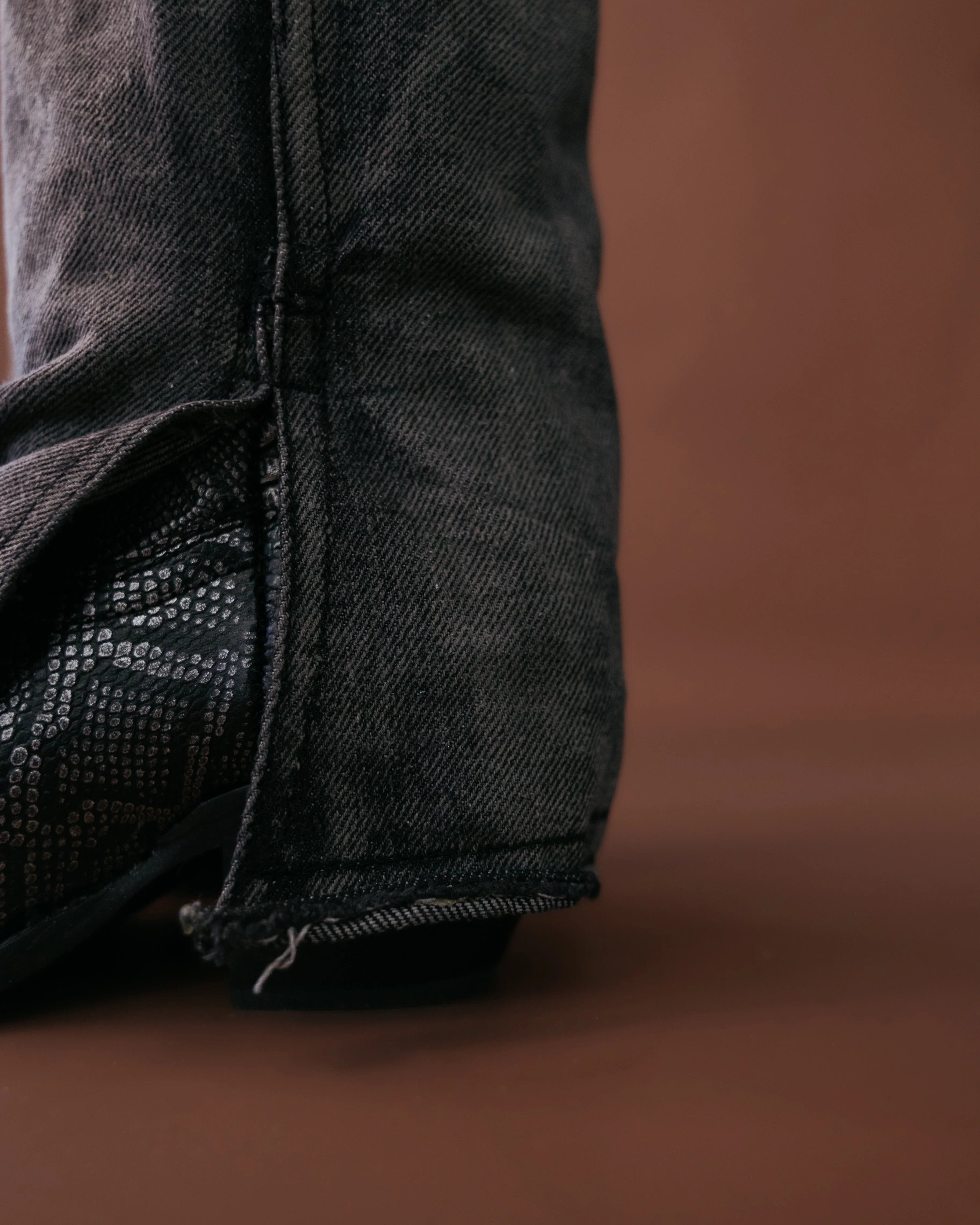 Black denim jeans with raw hem over black western boot on brown background