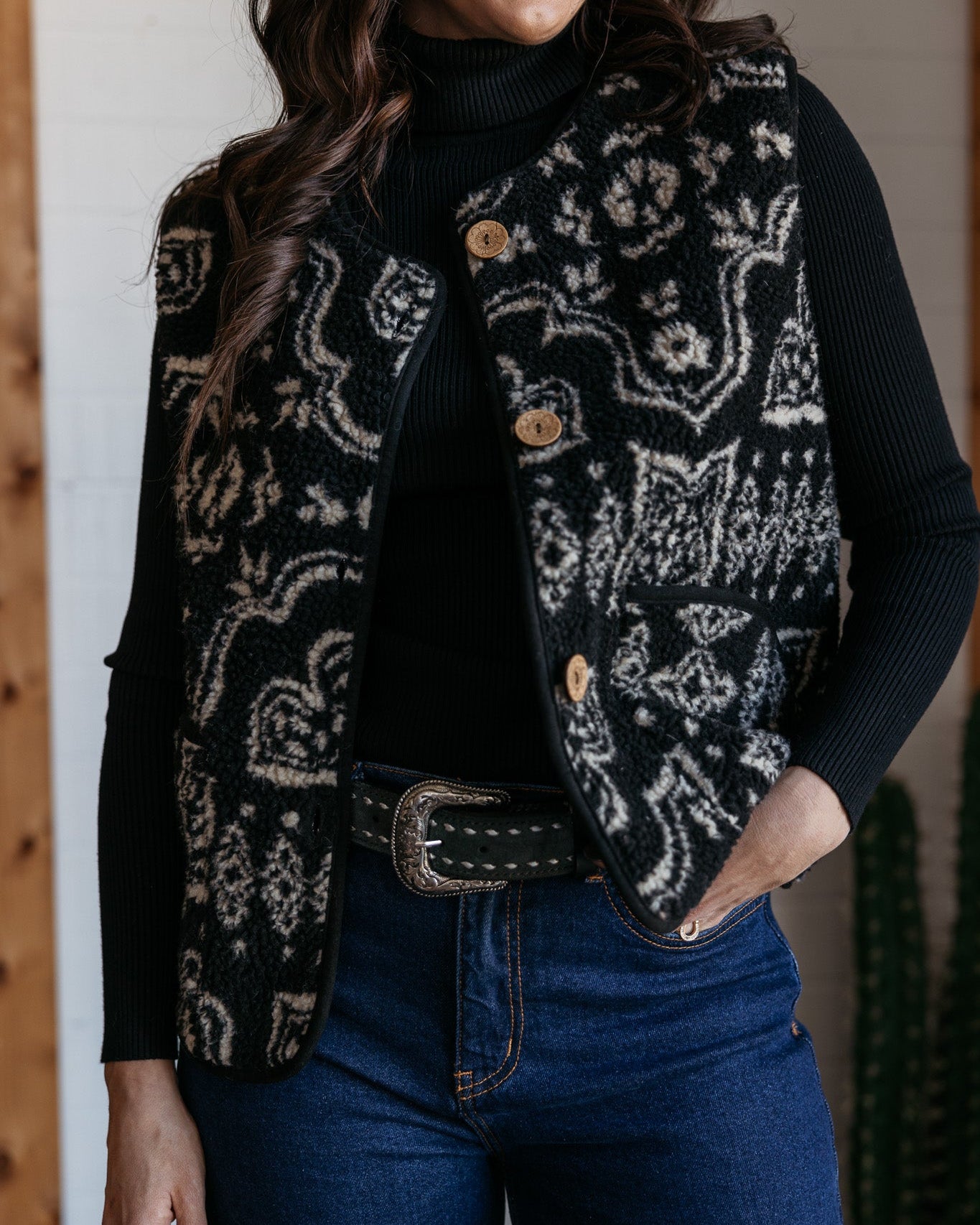 Woman in western boho patterned vest, black turtleneck, and high-rise blue jeans