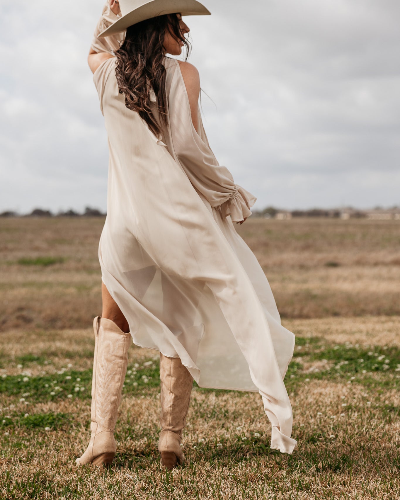 Woman in beige western boho dress and cowboy boots posing in a grassy field