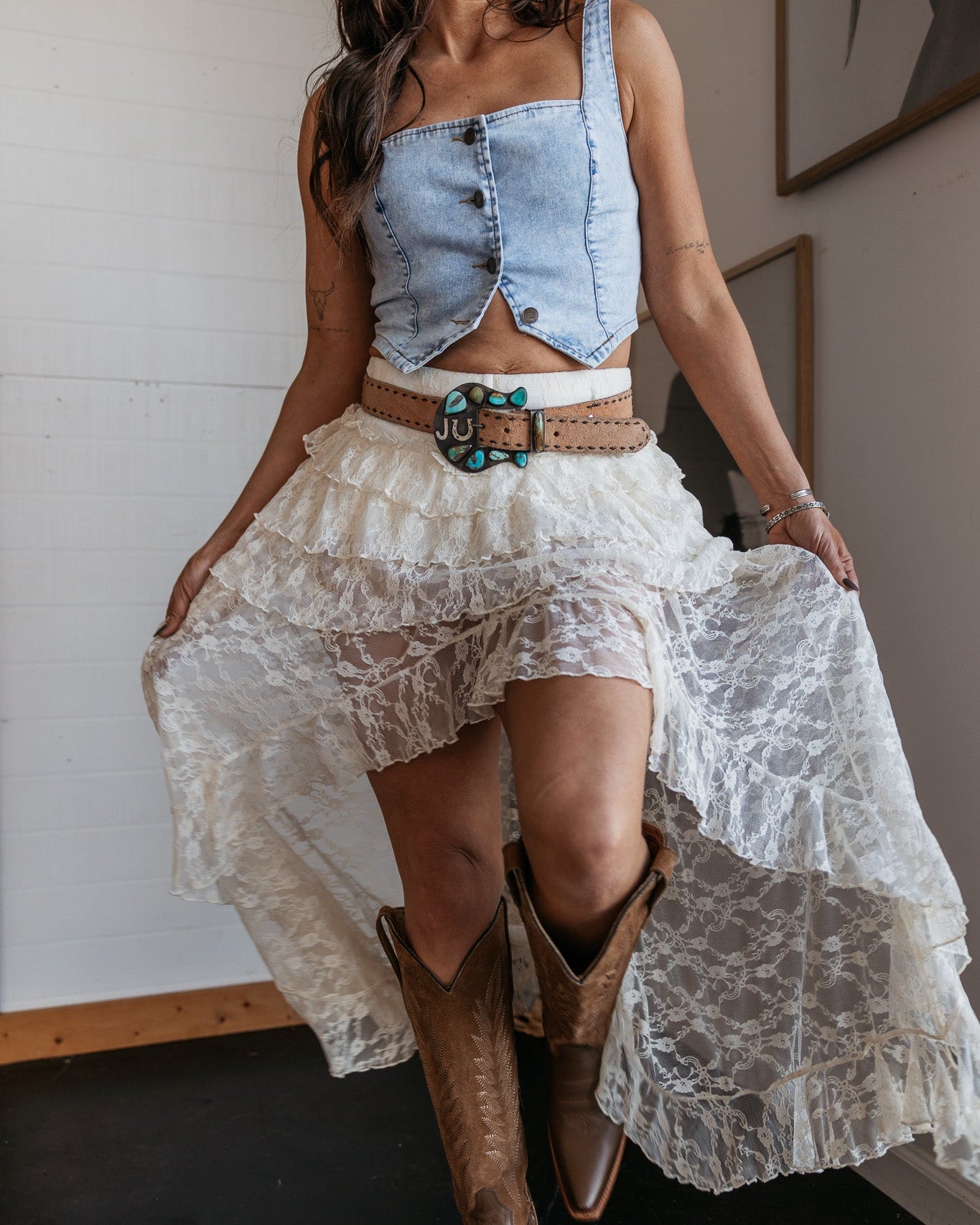 Woman in western boho outfit with denim crop top, lace skirt, turquoise belt, and cowboy boots
