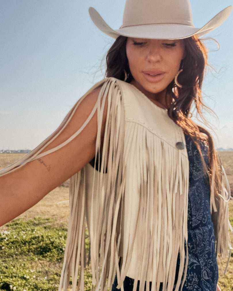 Woman in beige cowgirl hat and fringe western vest, boho rodeo style outdoors
