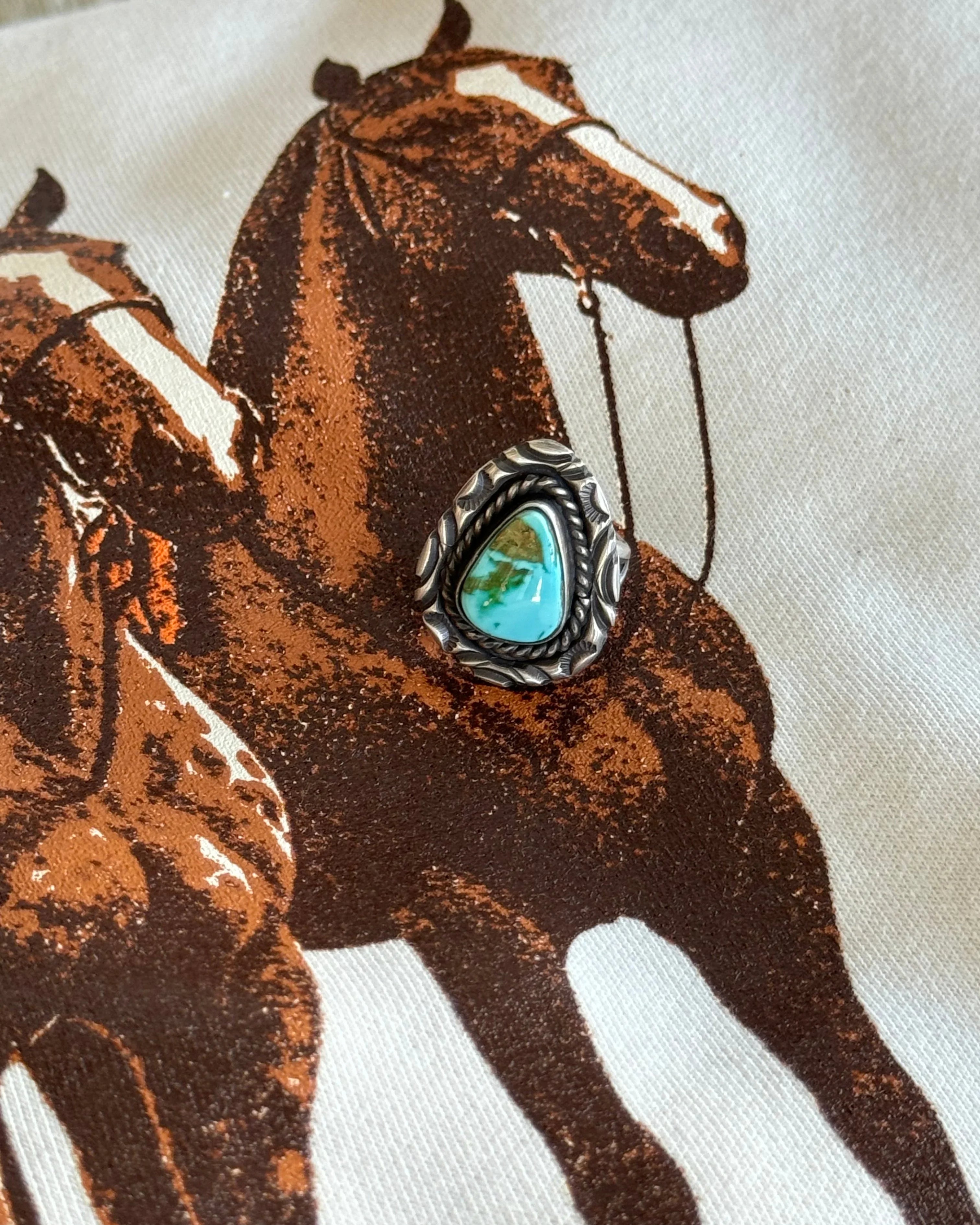 Turquoise western ring with silver engraved setting on cowboy horse print fabric