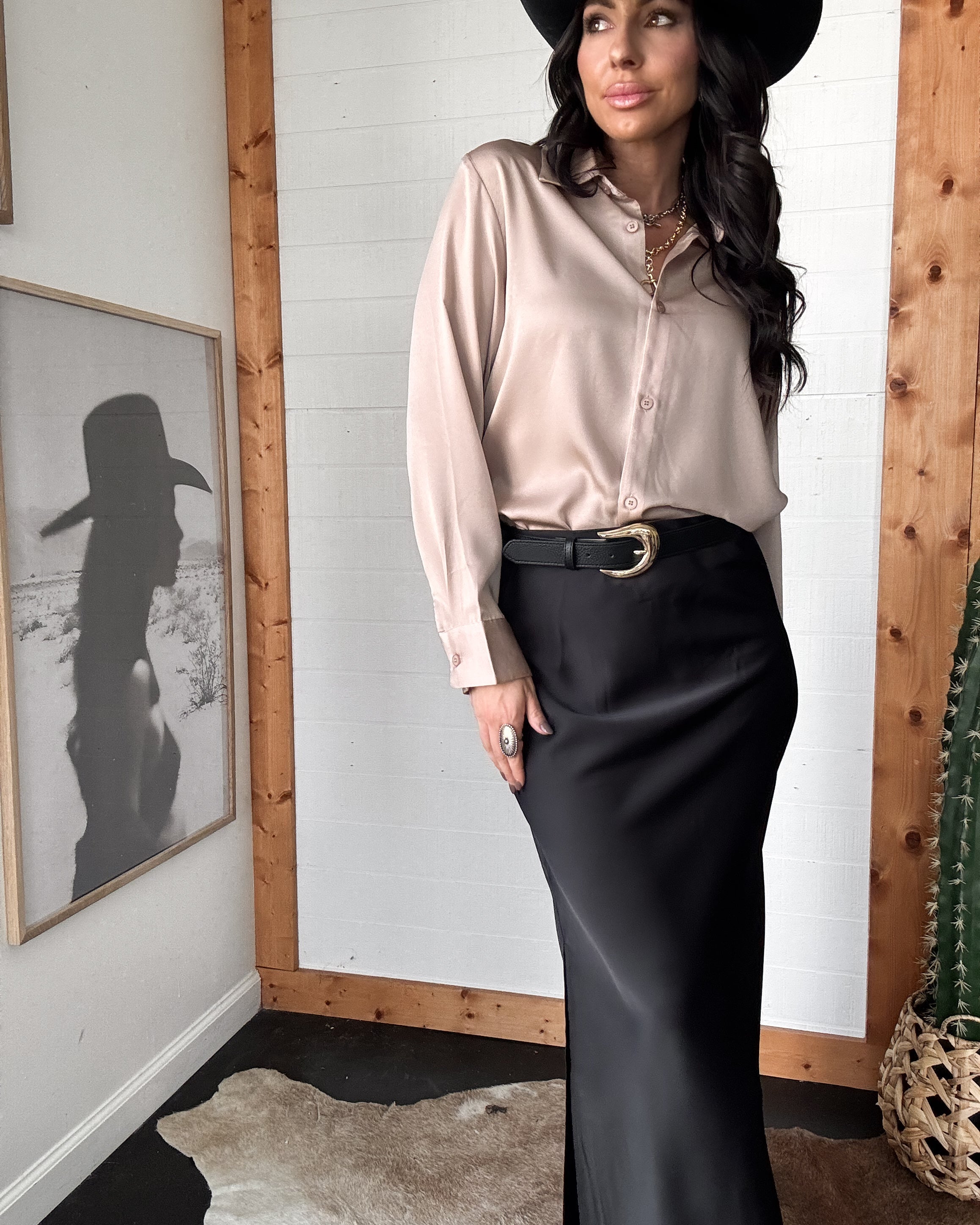 Woman in western boho outfit with black cowboy hat, silky blouse, black maxi skirt and belt