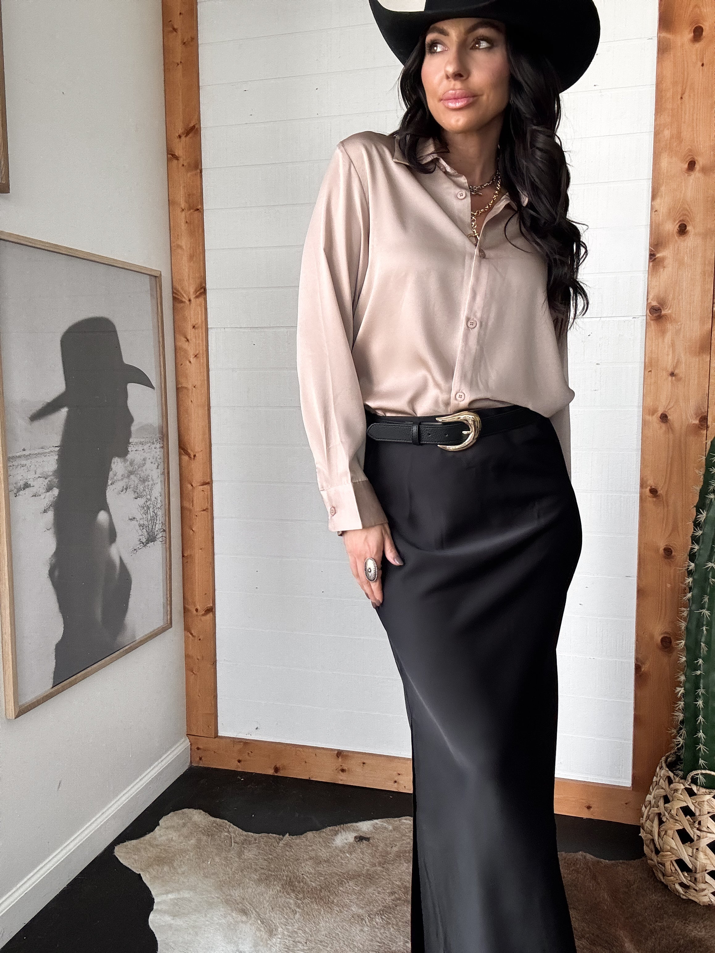 Woman in western boho outfit with black cowboy hat, silky blouse, black maxi skirt and belt