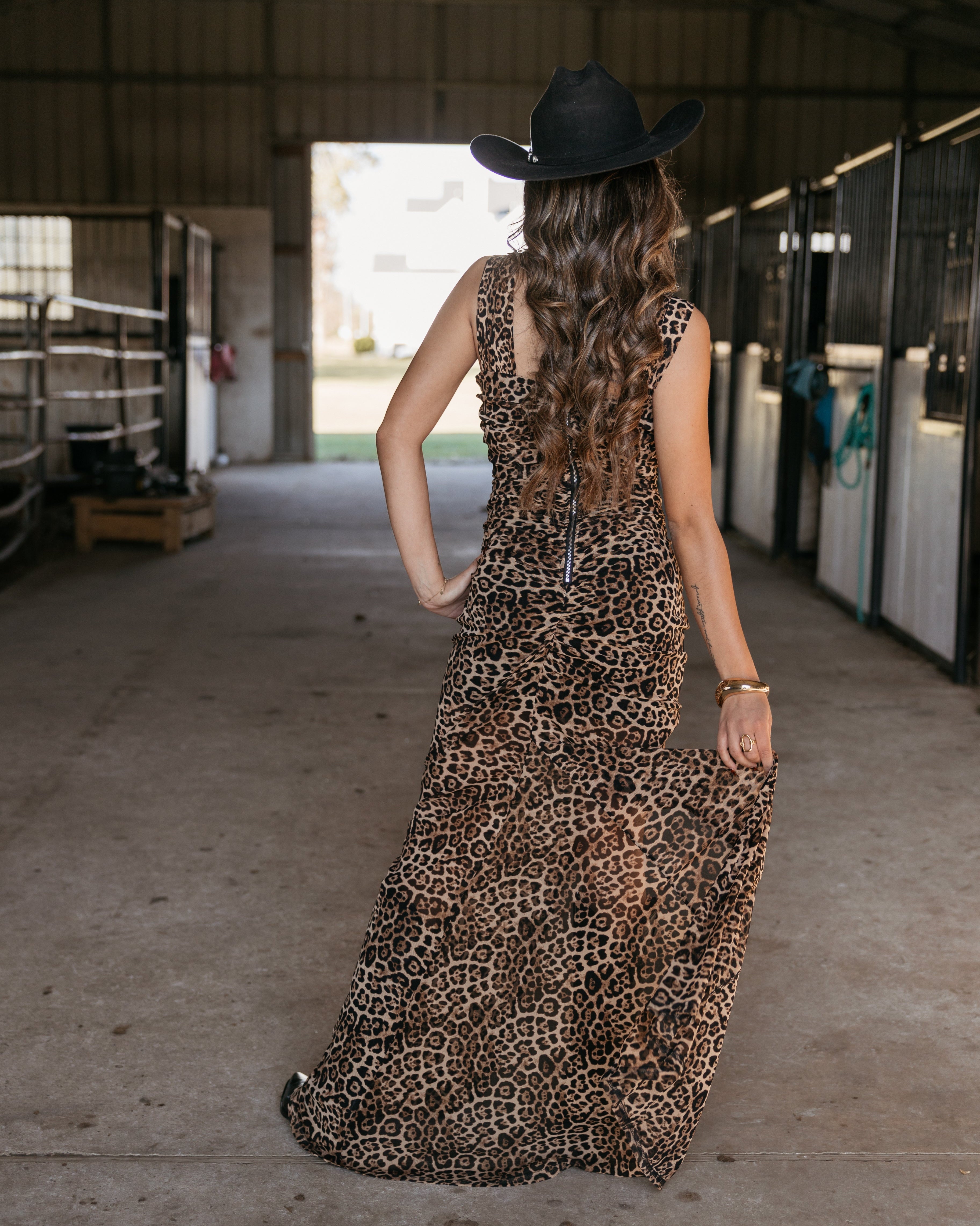 Woman in leopard print western dress and black cowboy hat standing in barn aisle