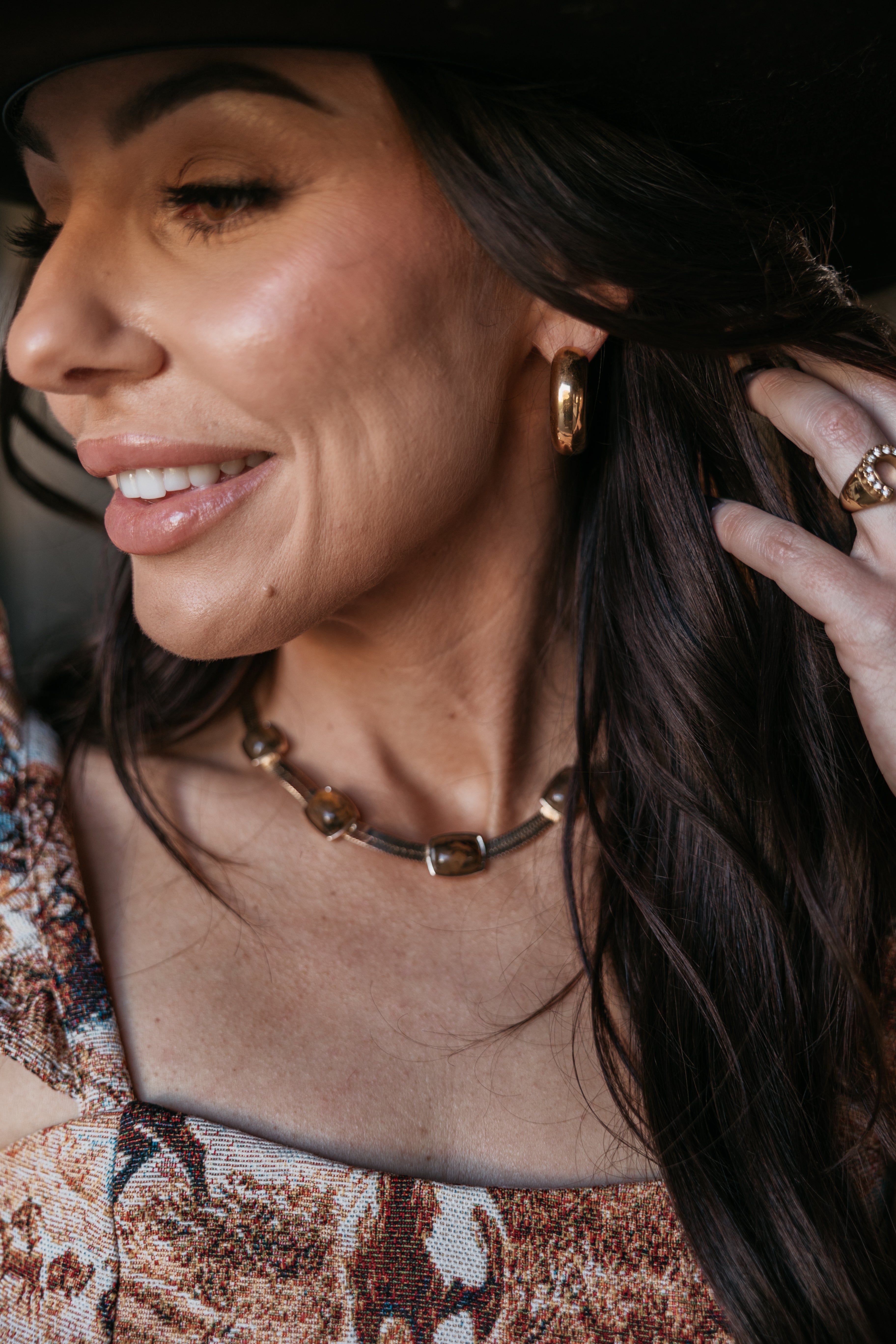 Smiling woman in western boho outfit with gold hoop earrings, ring, and chunky necklace