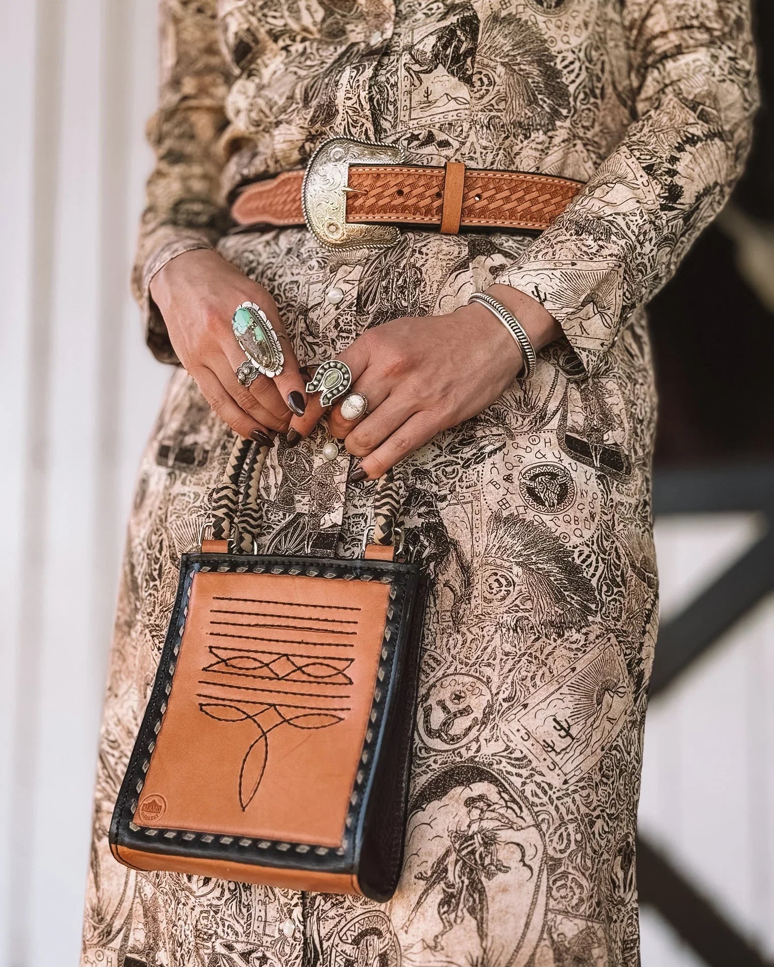 Western boho outfit with tooled leather belt, graphic dress, turquoise rings, and stitched purse