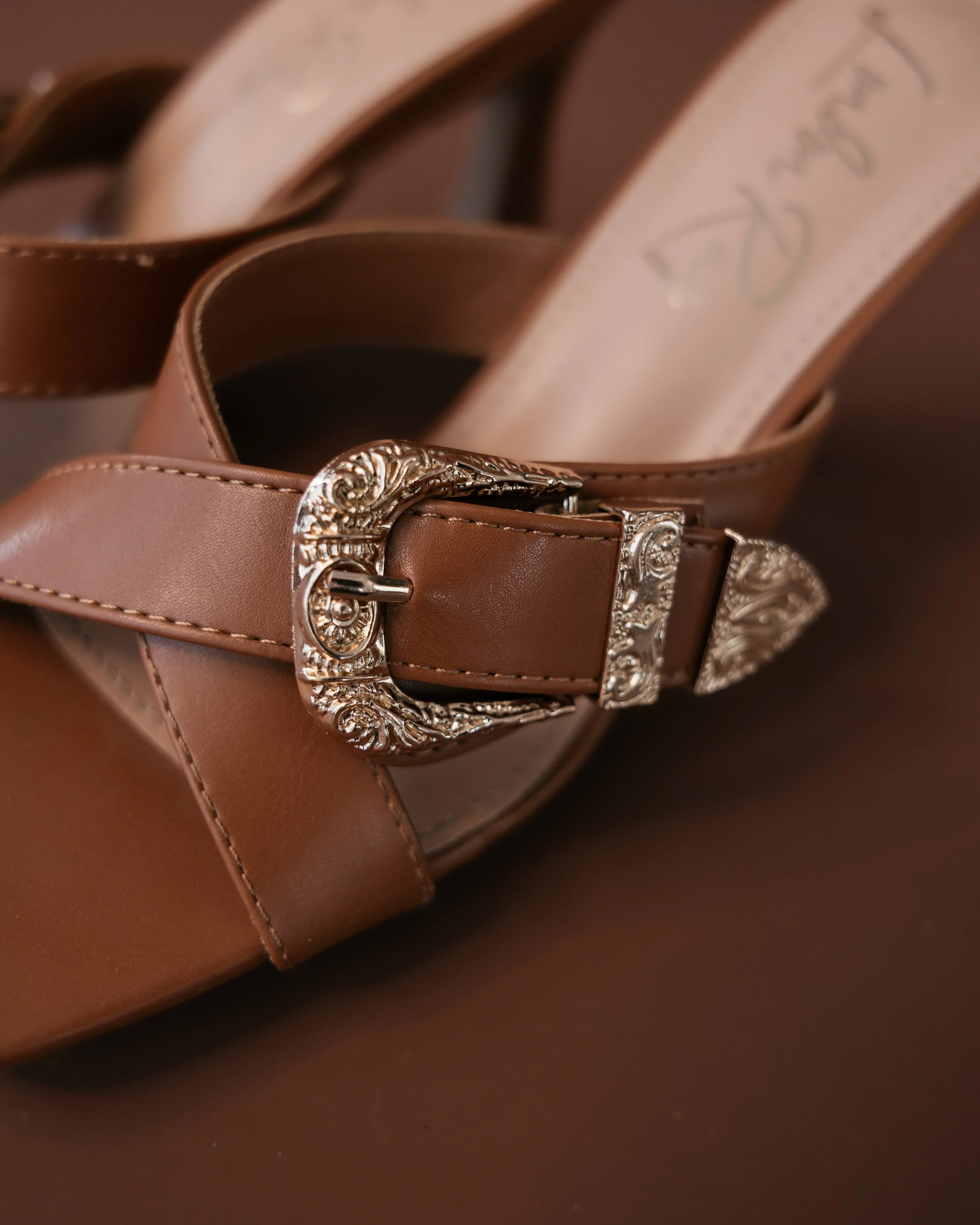 Brown western sandal with silver engraved buckle, boho cowgirl footwear on brown background