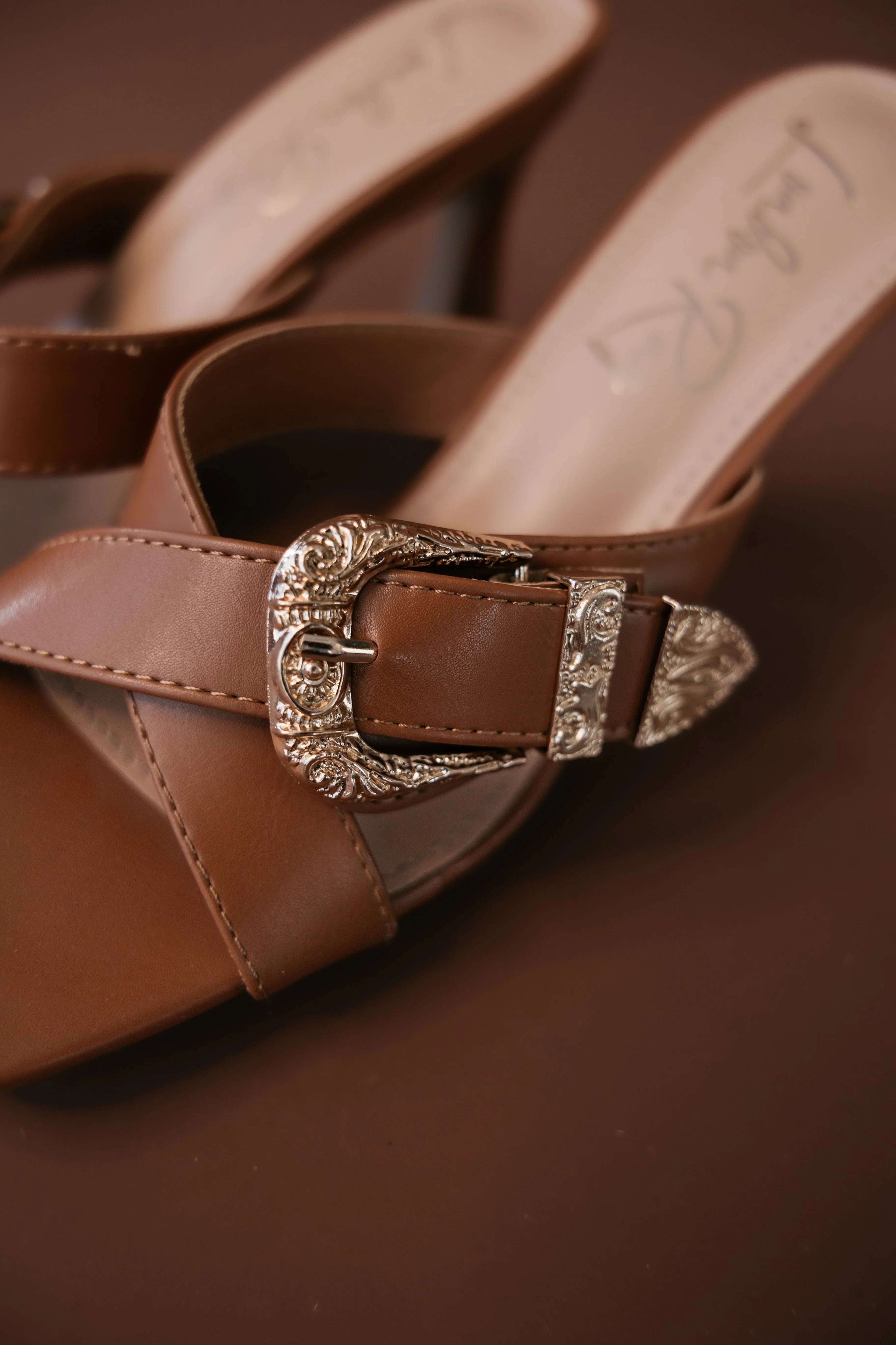 Brown western sandal with silver engraved buckle, boho cowgirl footwear on brown background
