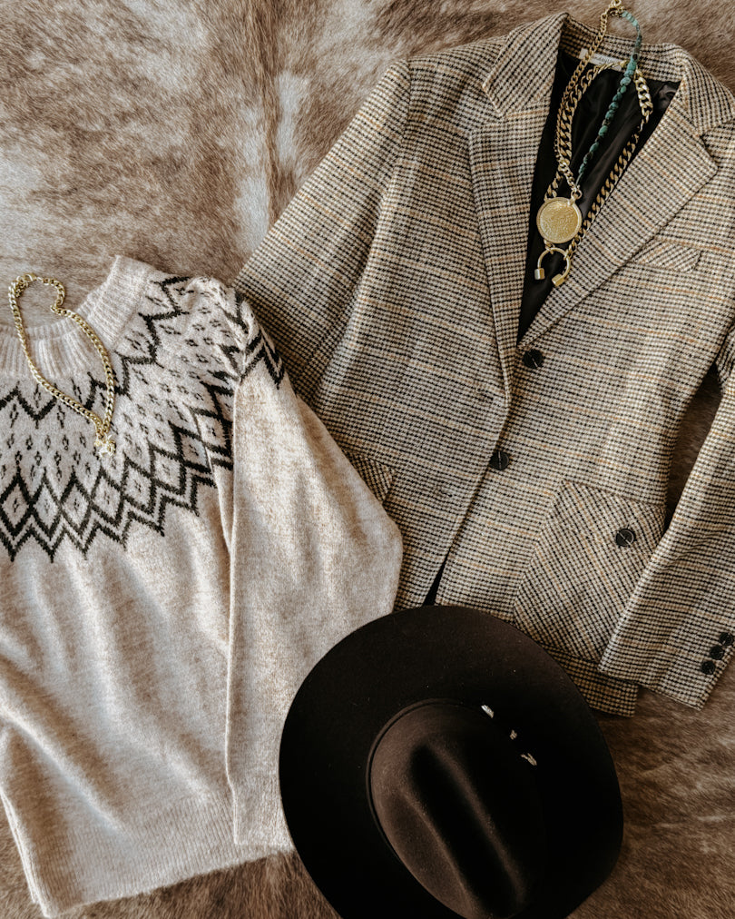 Gray checkered blazer, black and white patterned shirt, black hat, and gold necklace on a textured surface.