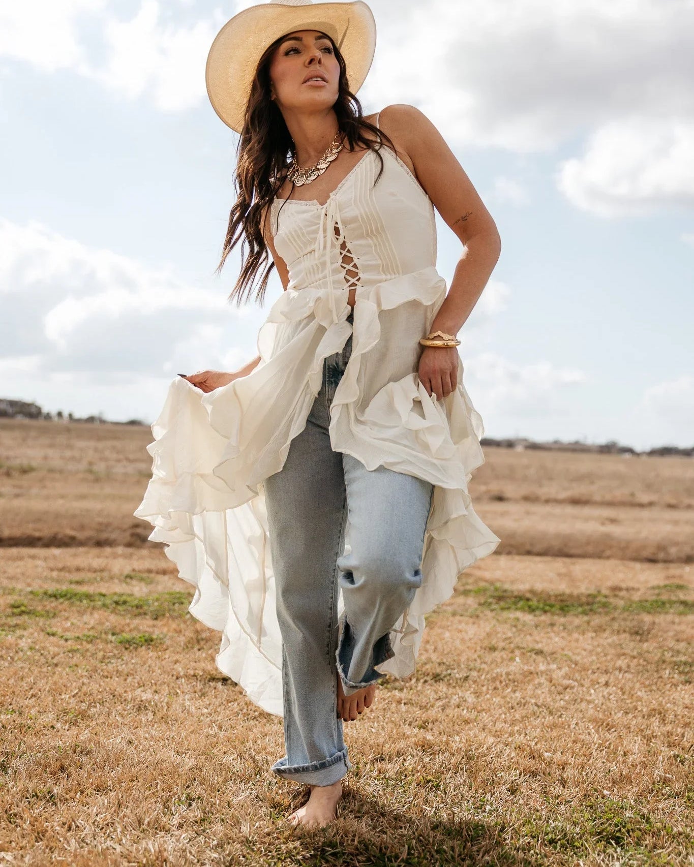 Woman in a cowboy hat wearing a boho western ruffle top and jeans in a rustic field