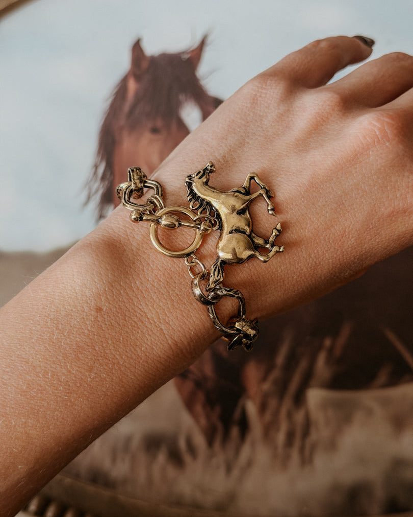 Western horse charm bracelet on wrist with galloping horse artwork in background