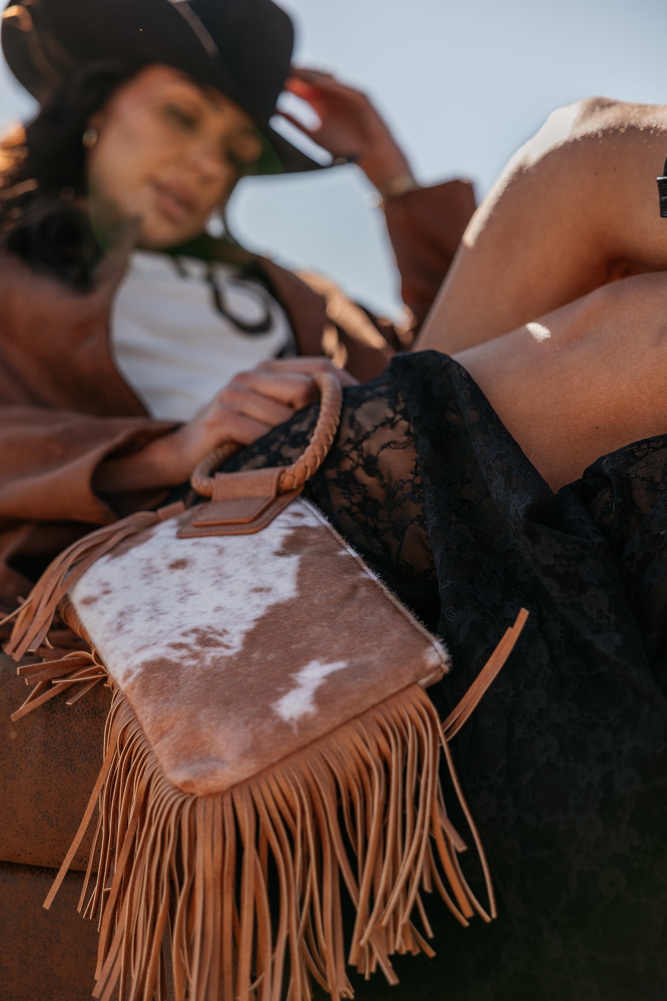 Cowgirl holding western fringe cowhide purse, black lace skirt, brown jacket, and hat