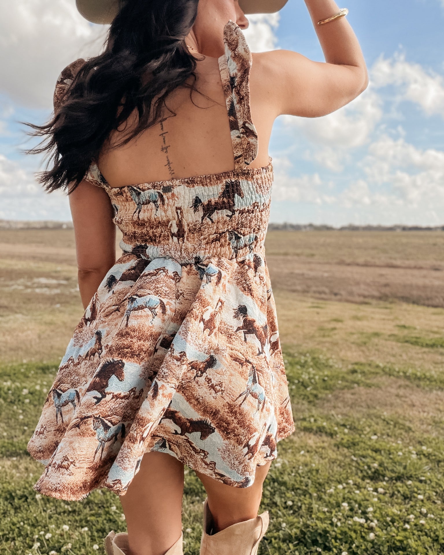 Woman in a western horse print sundress, cowboy boots, and hat in a country field
