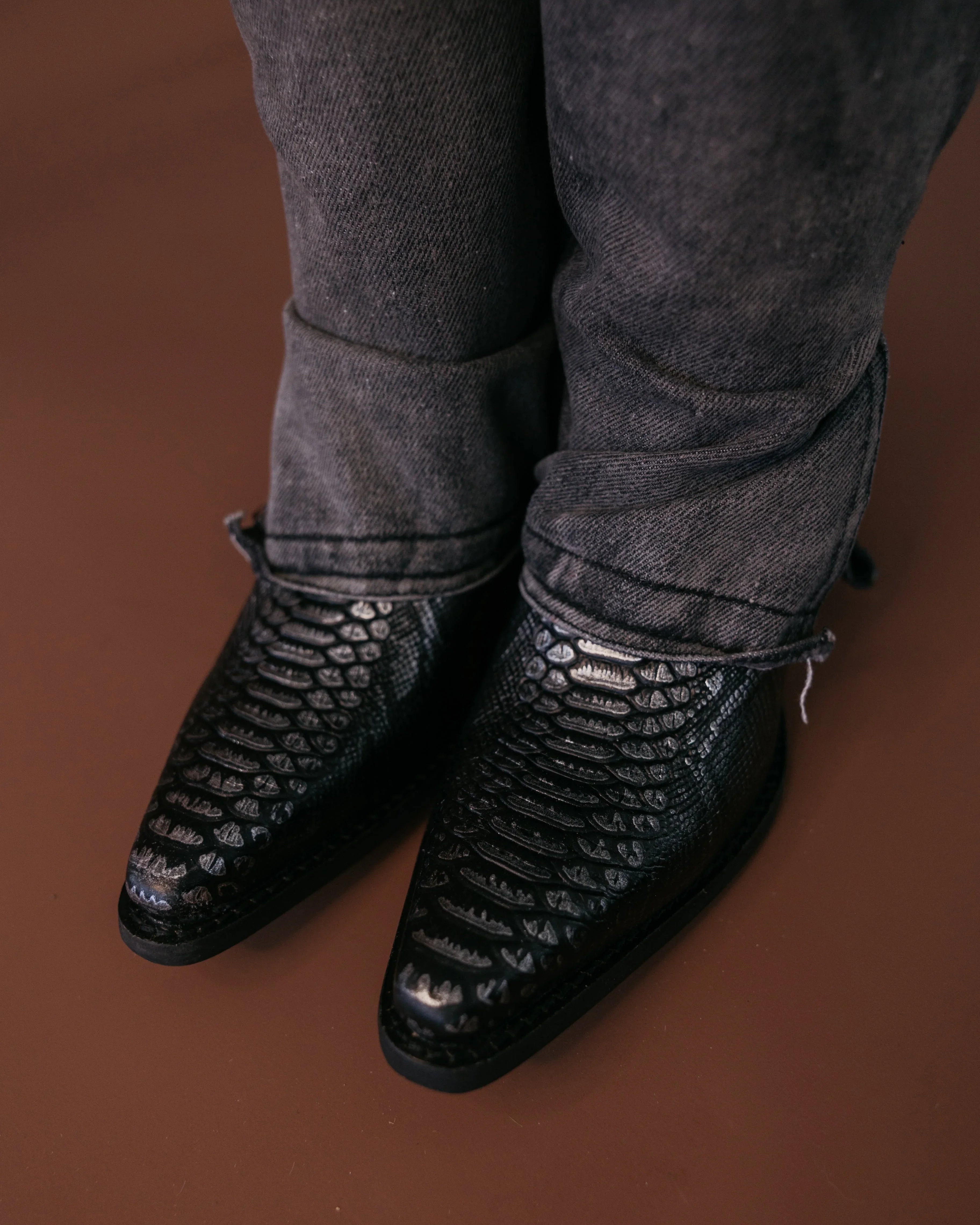 Black snakeskin western cowboy boots with pointed toes and distressed black jeans