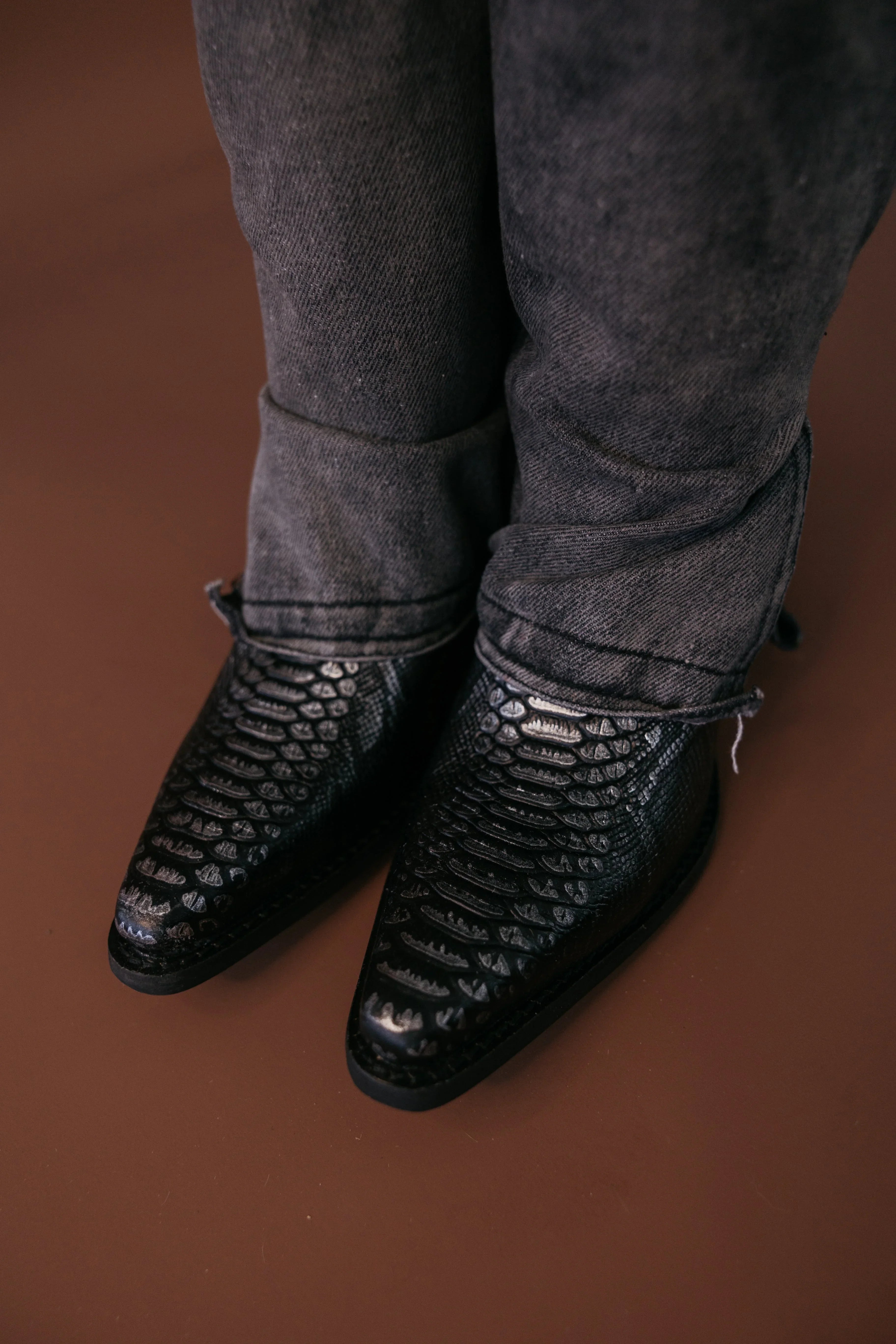 Black snakeskin western cowboy boots with pointed toes and distressed black jeans