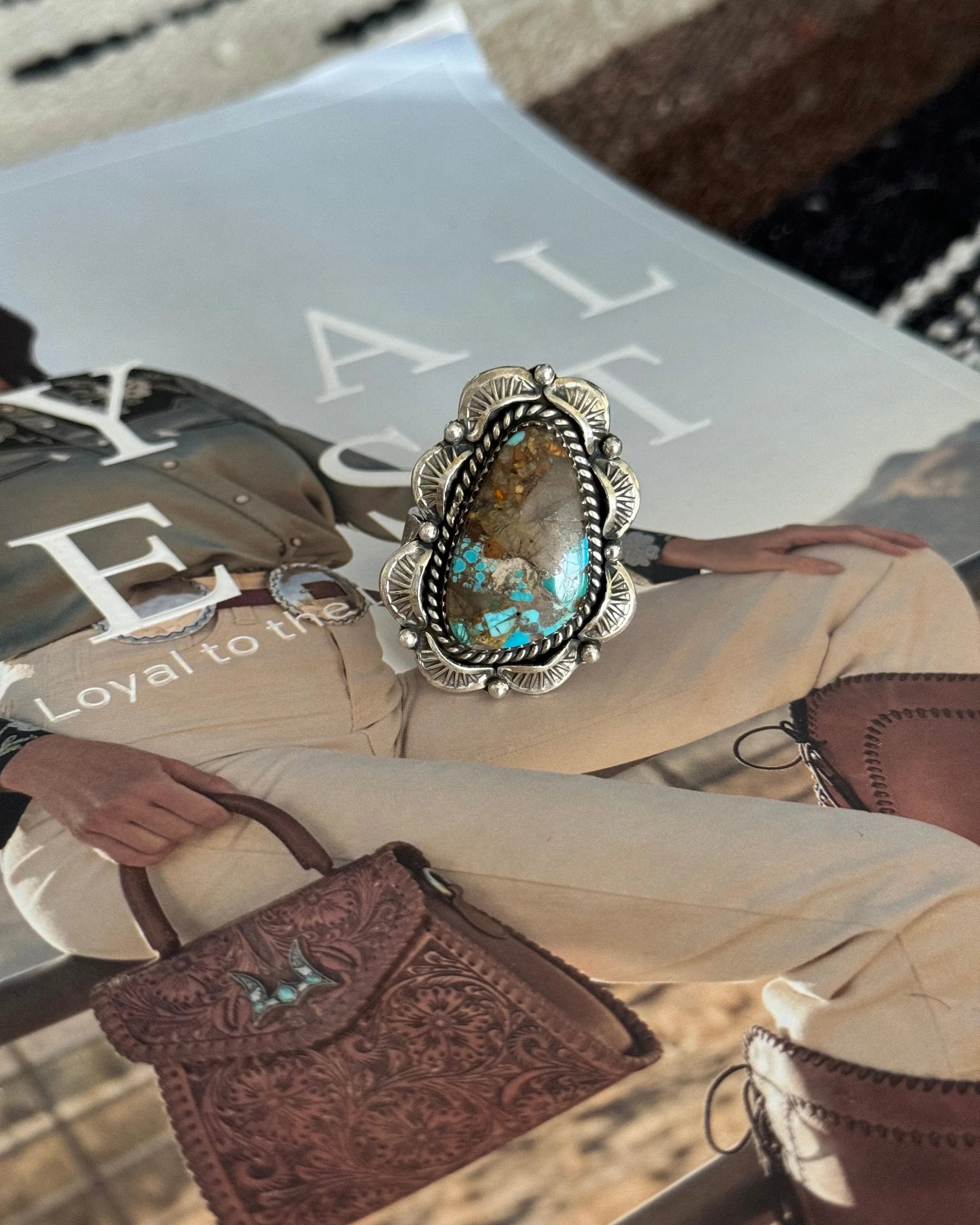 Western boho turquoise statement ring with engraved silver setting on magazine background