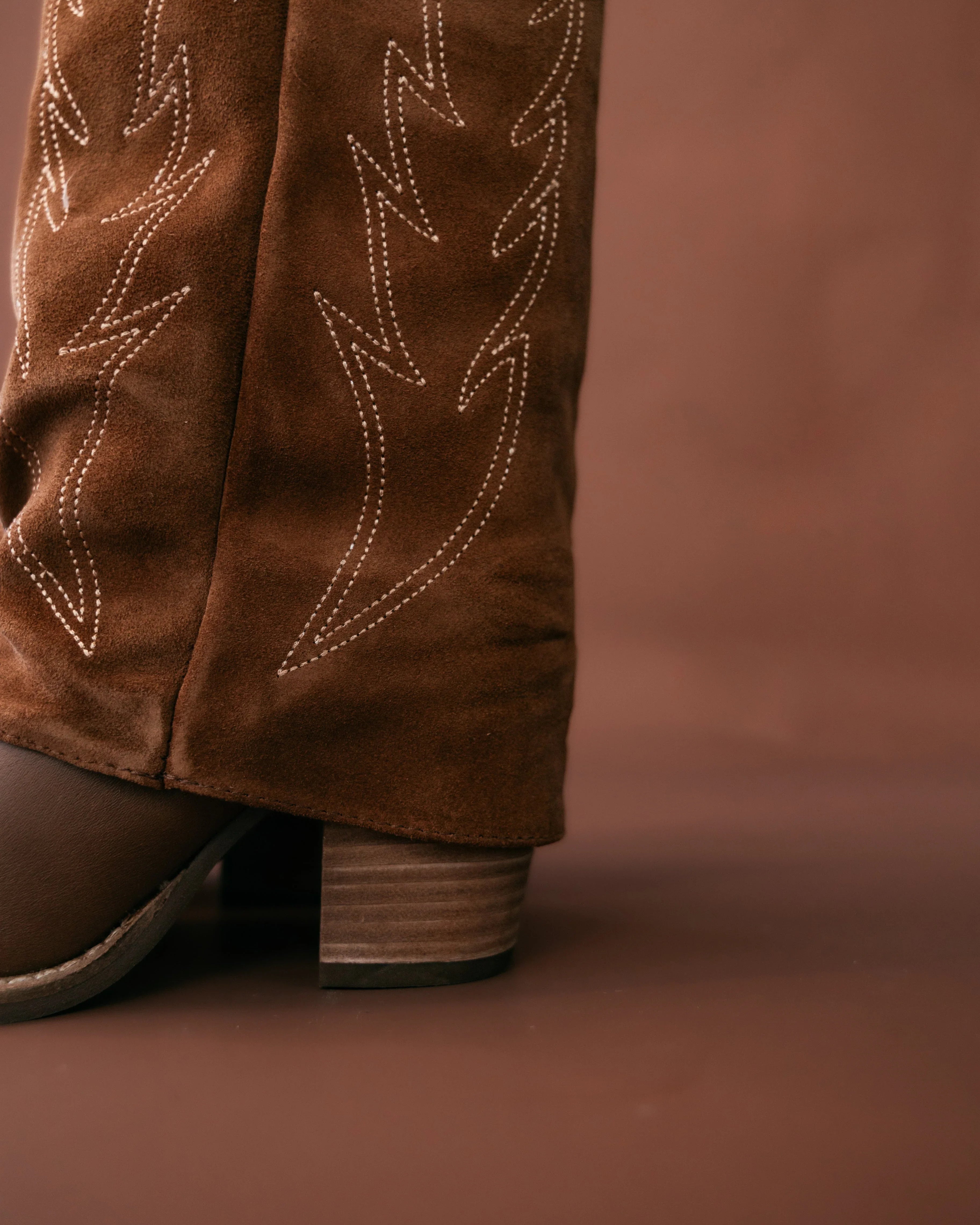 Brown suede boot with decorative stitching on a brown background
