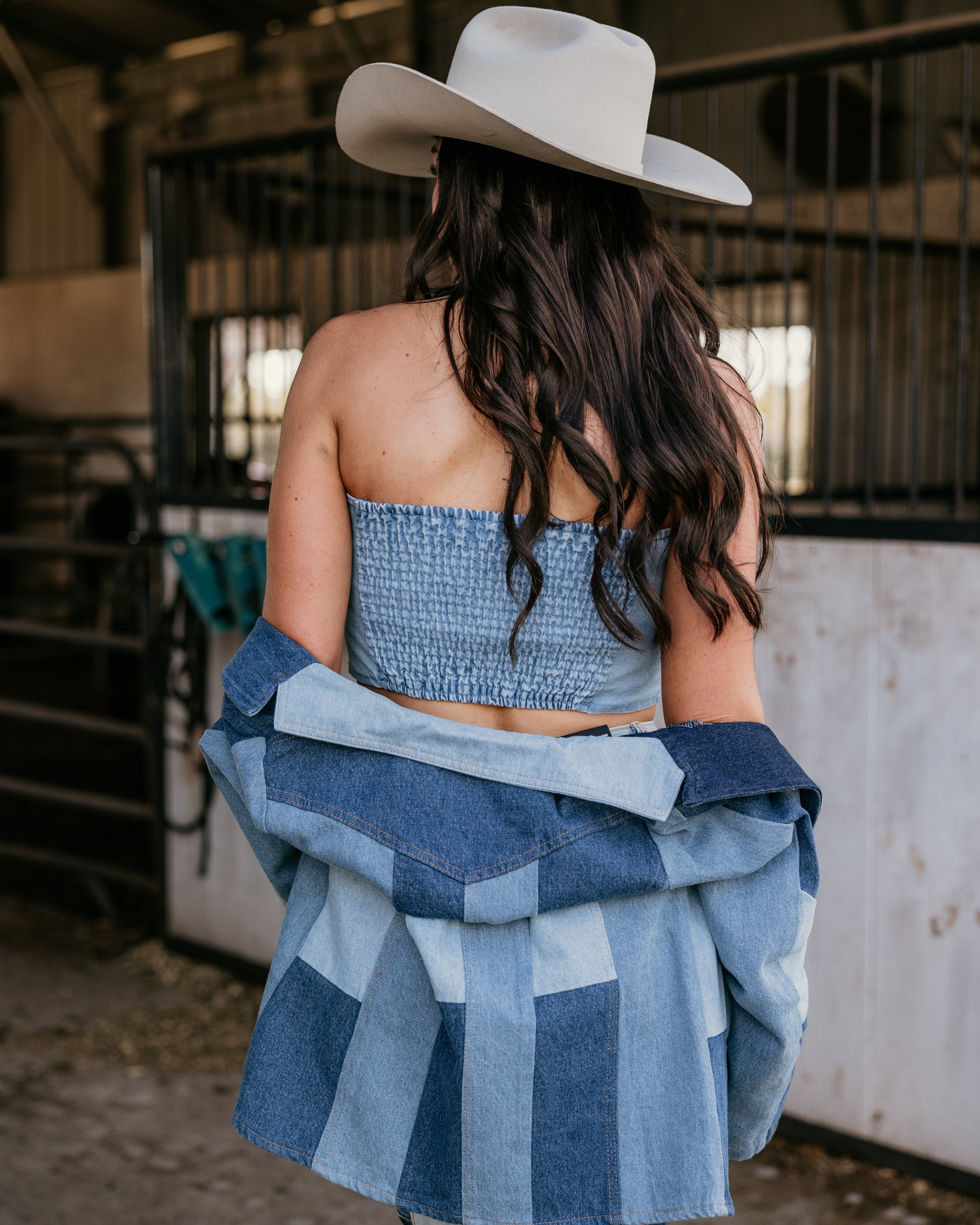 Woman in denim patchwork outfit and cowboy hat, western boho style in barn setting