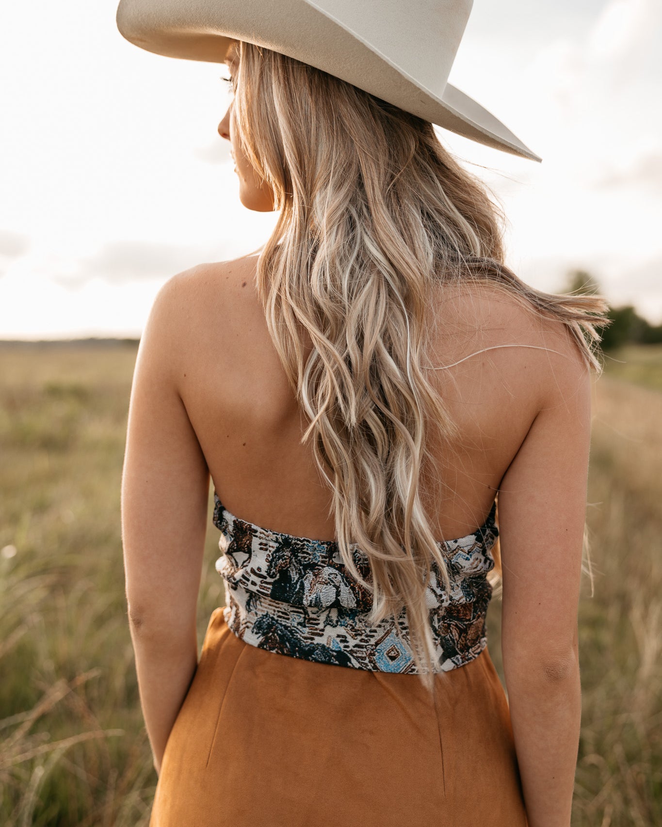 women wearing western halter top with low back and a camel skirt standing in a field.