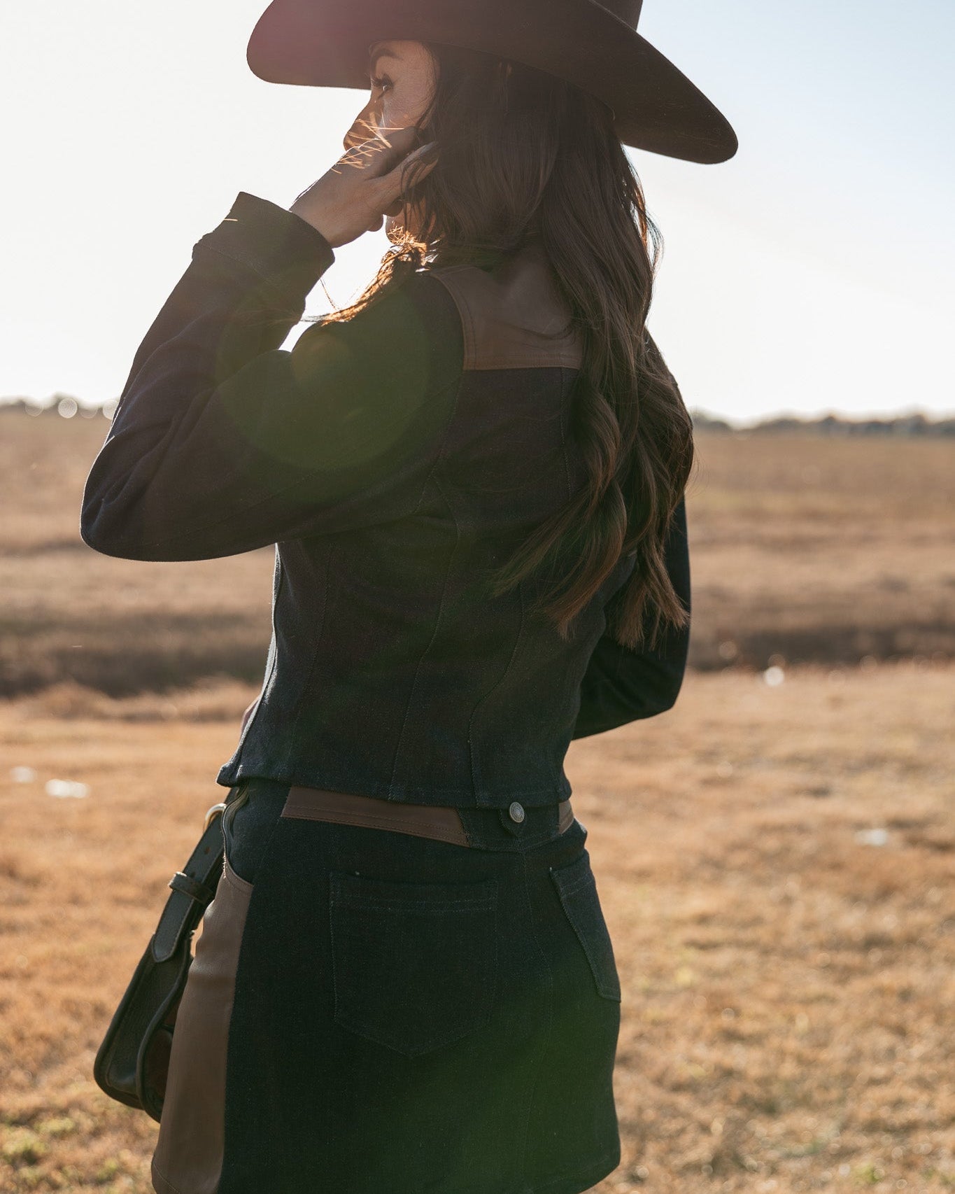 Woman in western boho outfit with black hat and jacket standing in a sunlit field