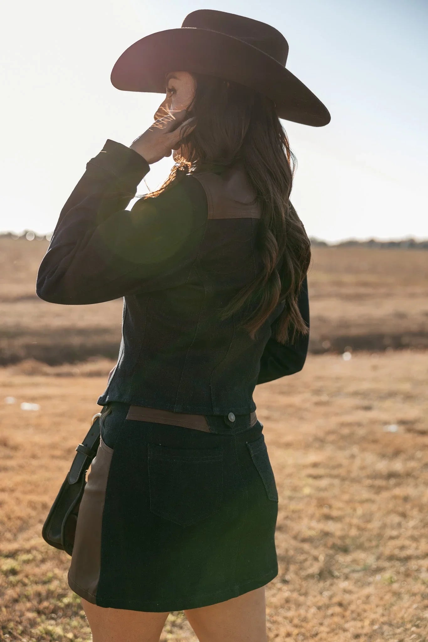 Woman in western boho outfit with black hat and jacket standing in a sunlit field