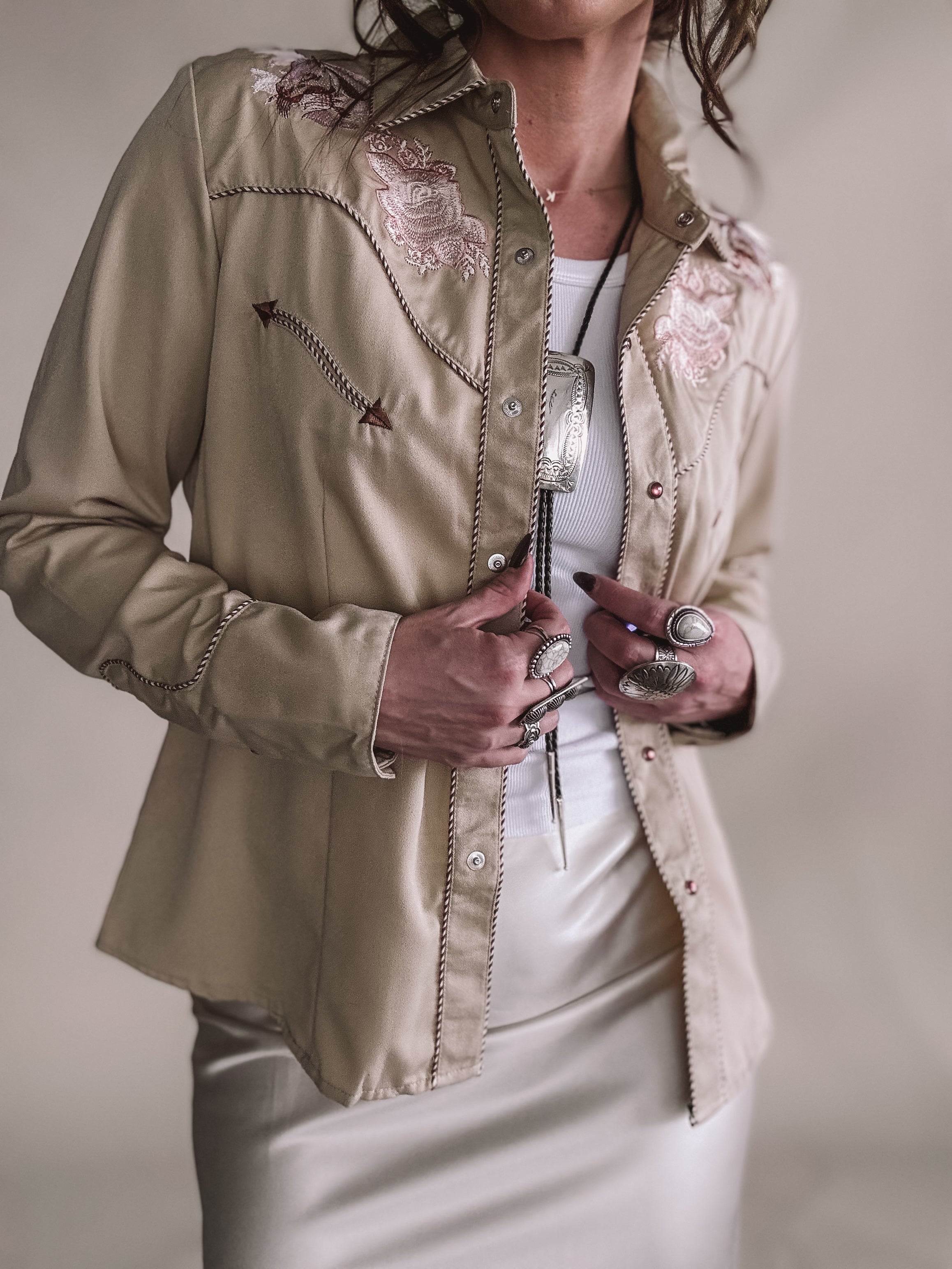 Woman wearing a beige western shirt with floral embroidery and silver jewelry.