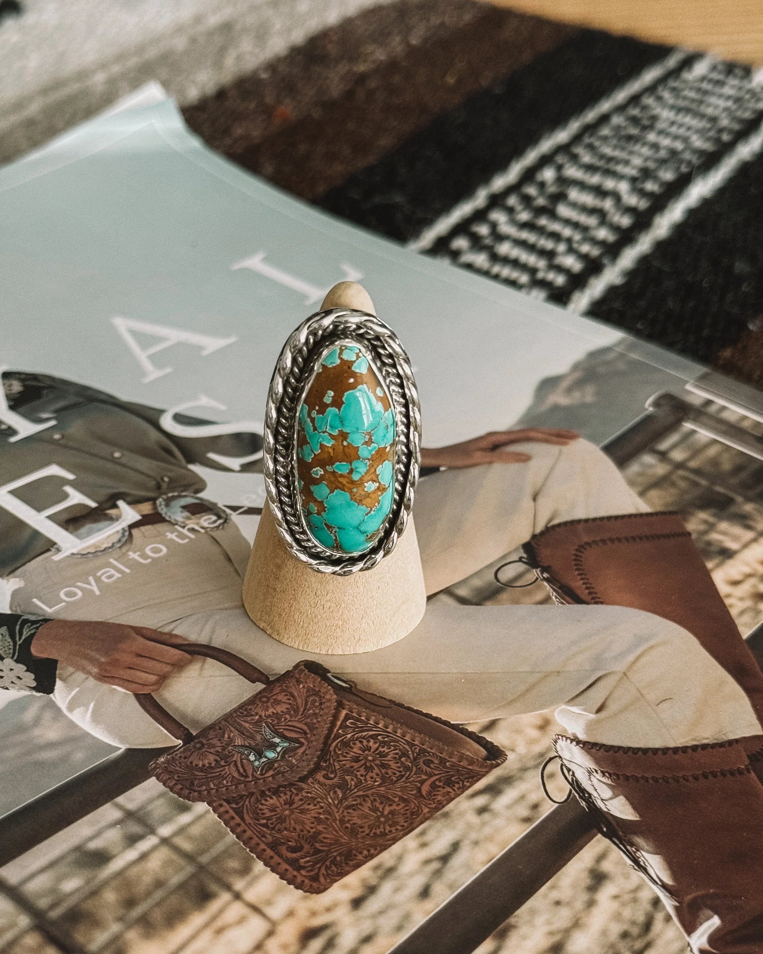 Turquoise and brown western boho ring with silver setting on wooden display, magazine background
