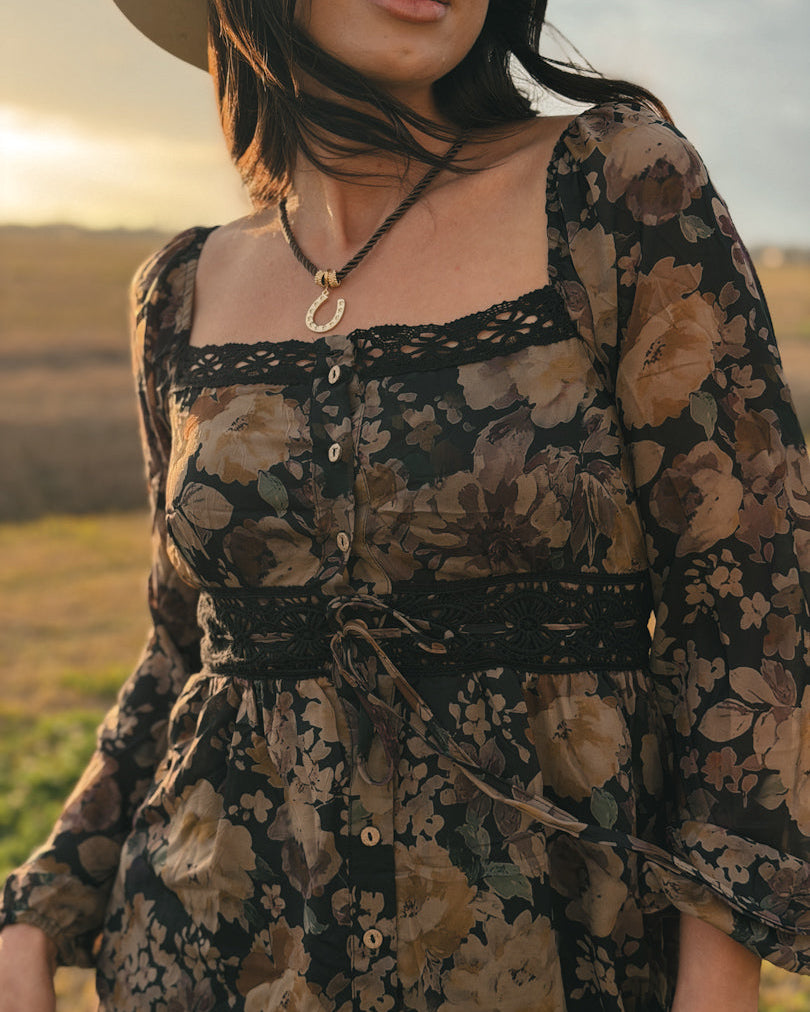 Woman in western floral boho dress with square neckline and horseshoe necklace outdoors