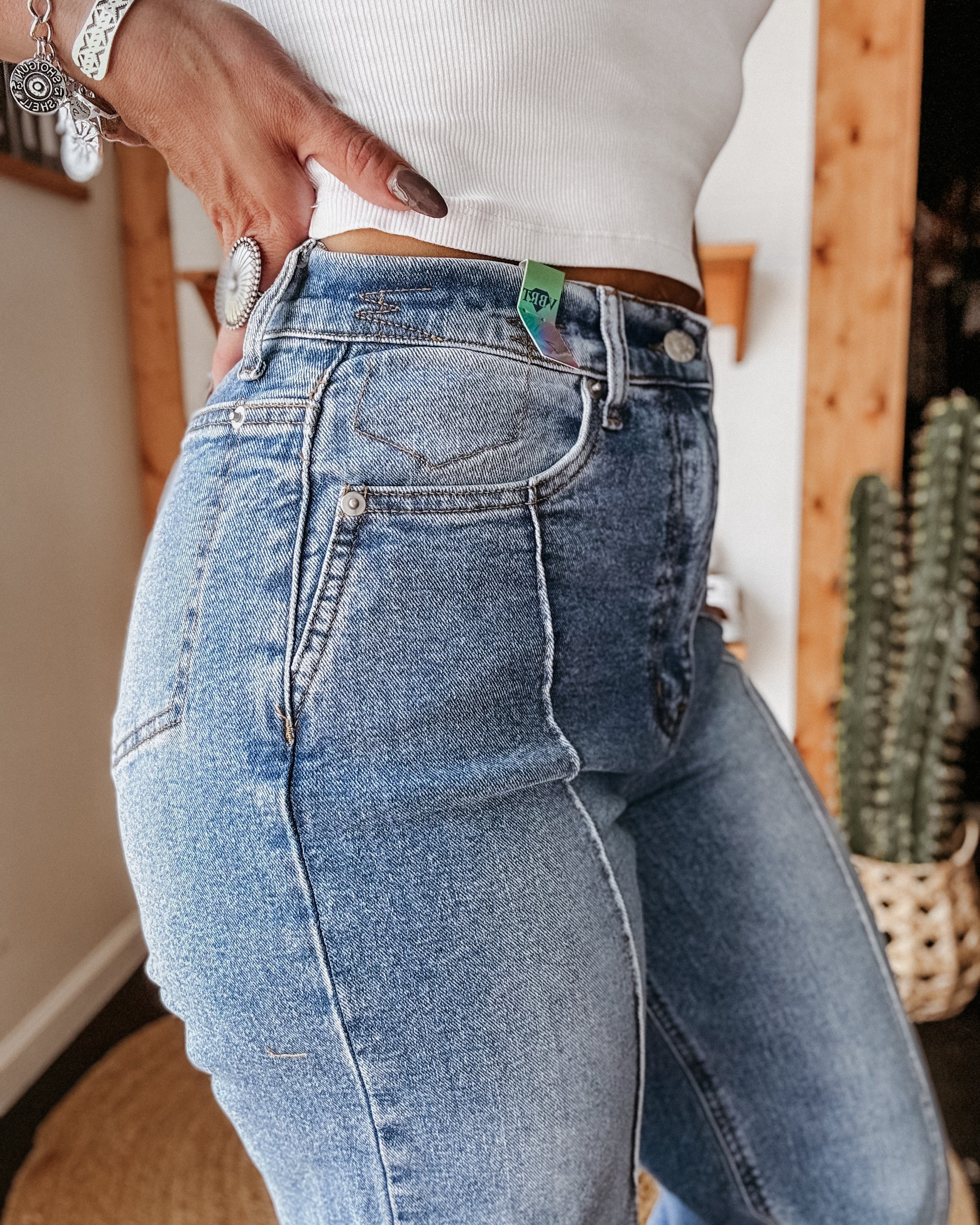 Woman wearing high-waisted blue western jeans and a white ribbed tank top indoors.